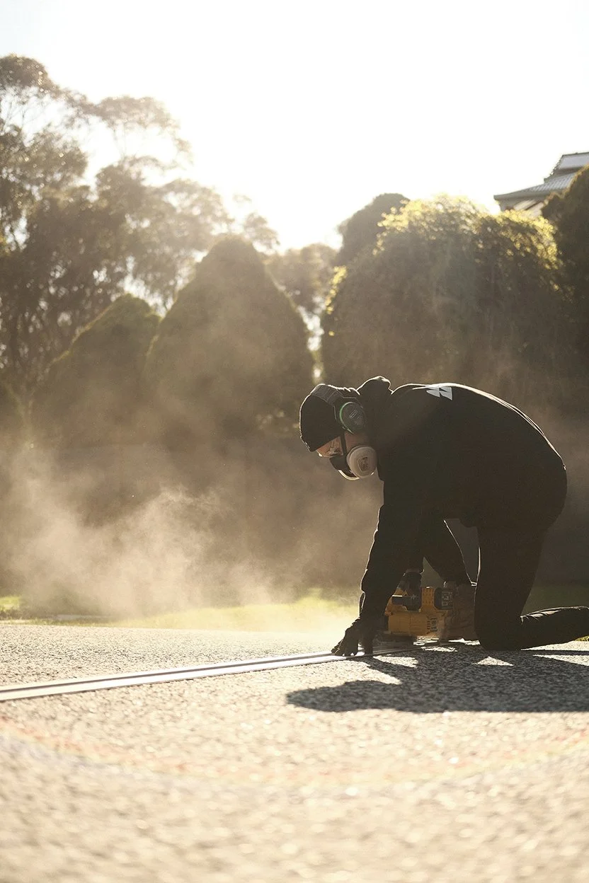 A worker kneeling on the road, welding the road surface with a welding machine, creating sparks in the sunlight.