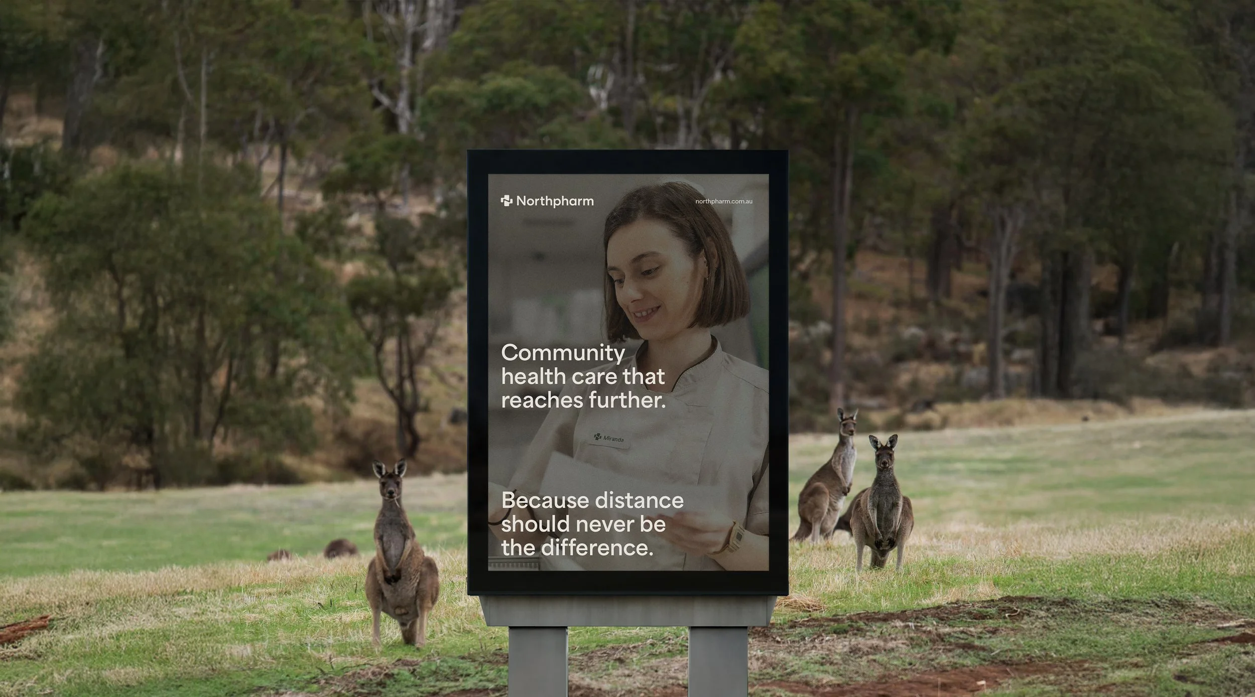 Digital outdoor billboard displaying a healthcare message with a portrait of a woman in medical attire, set against a grassy park with trees and kangaroos.