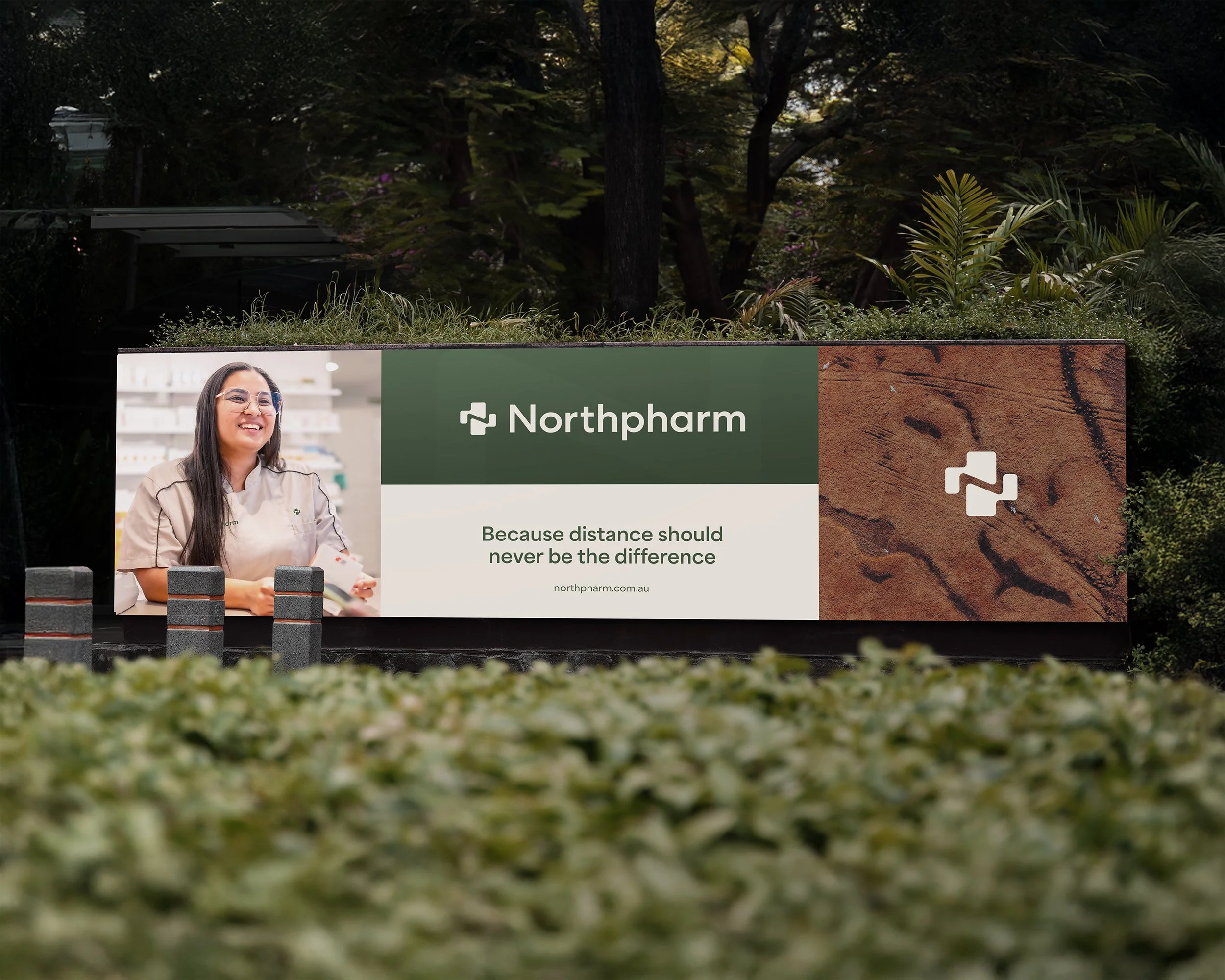 A large outdoor advertisement for Northpharm featuring a smiling woman in a pharmacy or medical setting, with the tagline 'Because distance should never be the difference' and the website northpharm.com.au, displayed against a backdrop of trees and greenery.