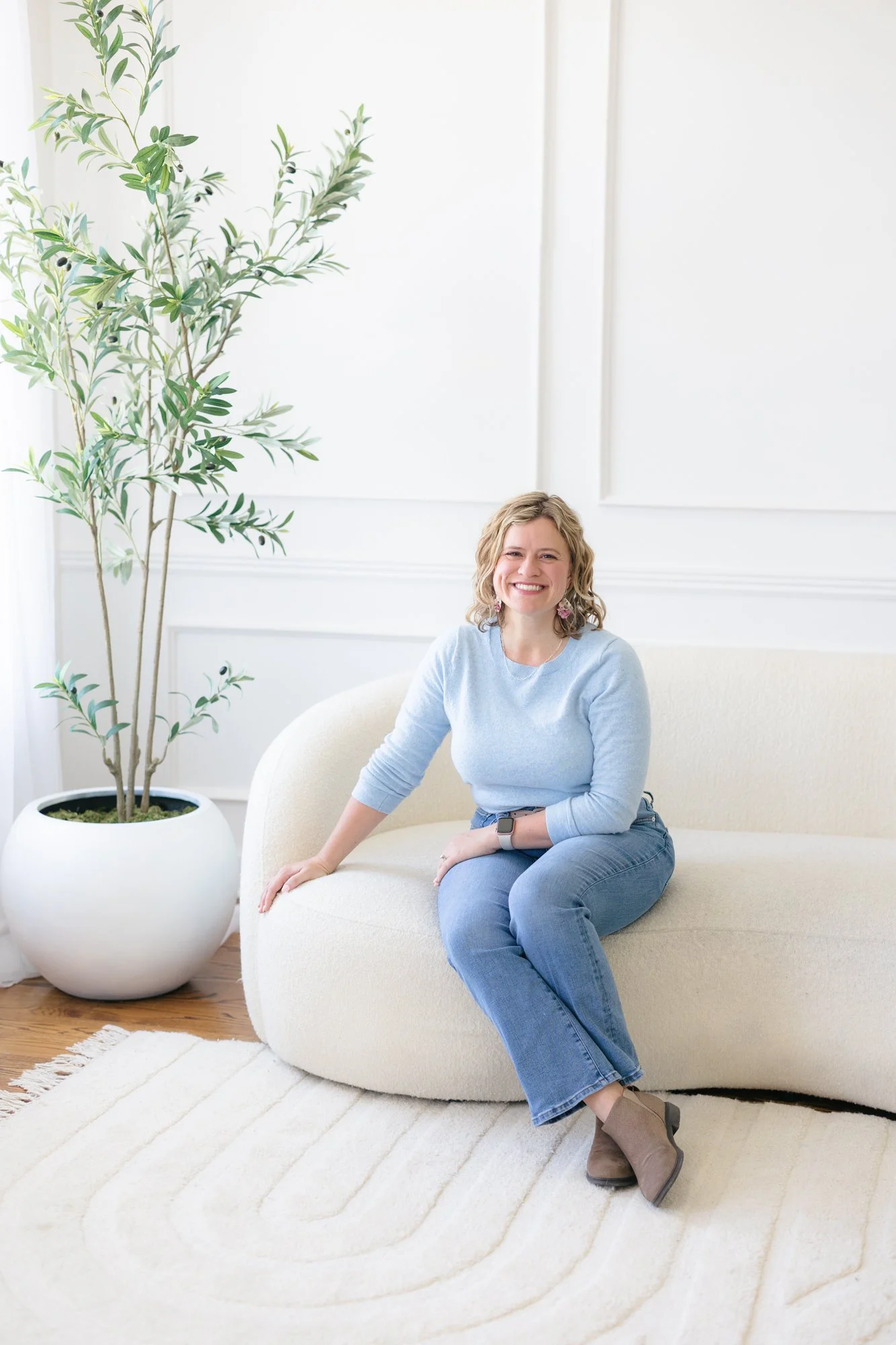 Dr. Amber Penn sitting on couch smiling with green floor plant next to her
