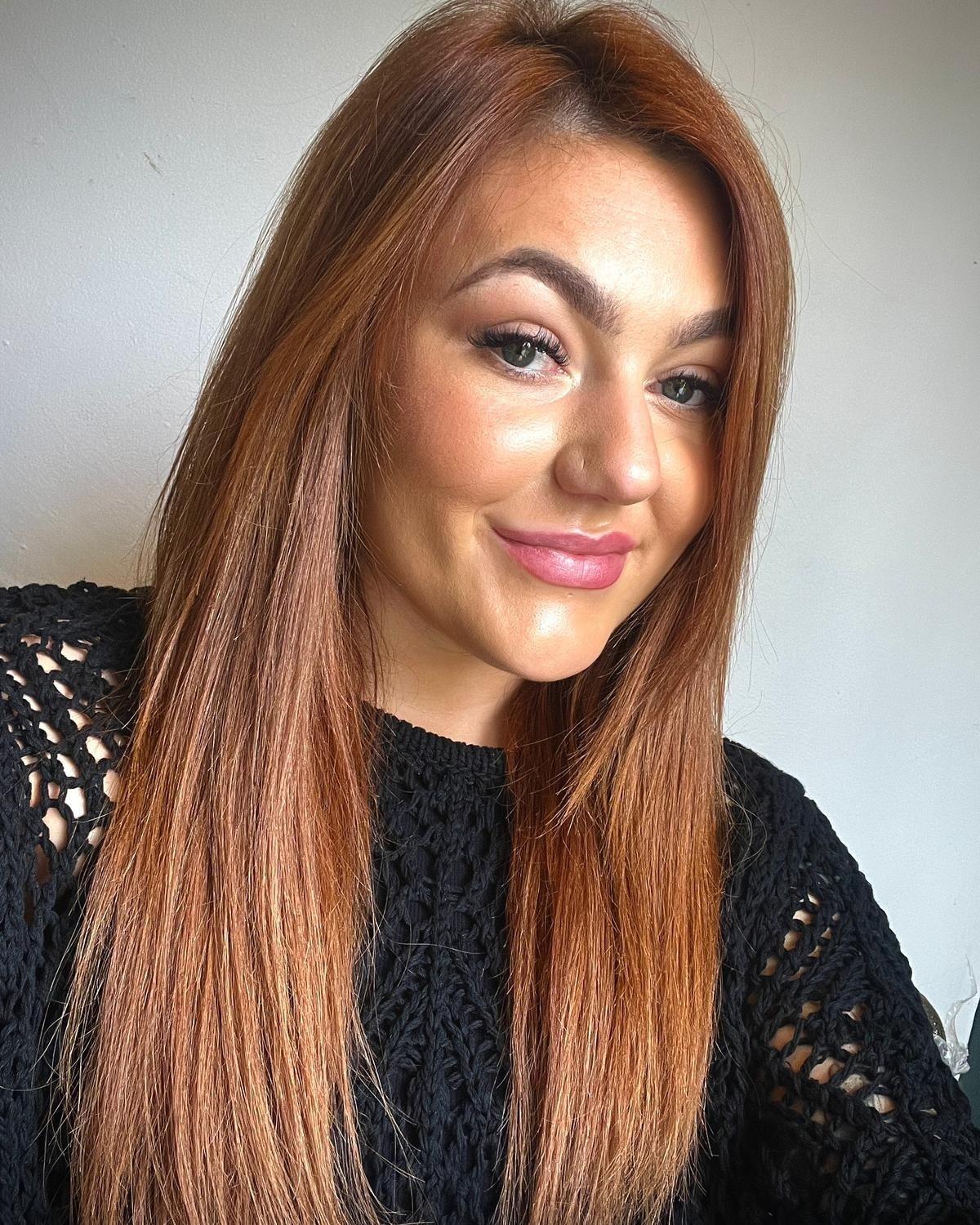 Woman with long reddish-brown hair and a black knitted sweater smiling.