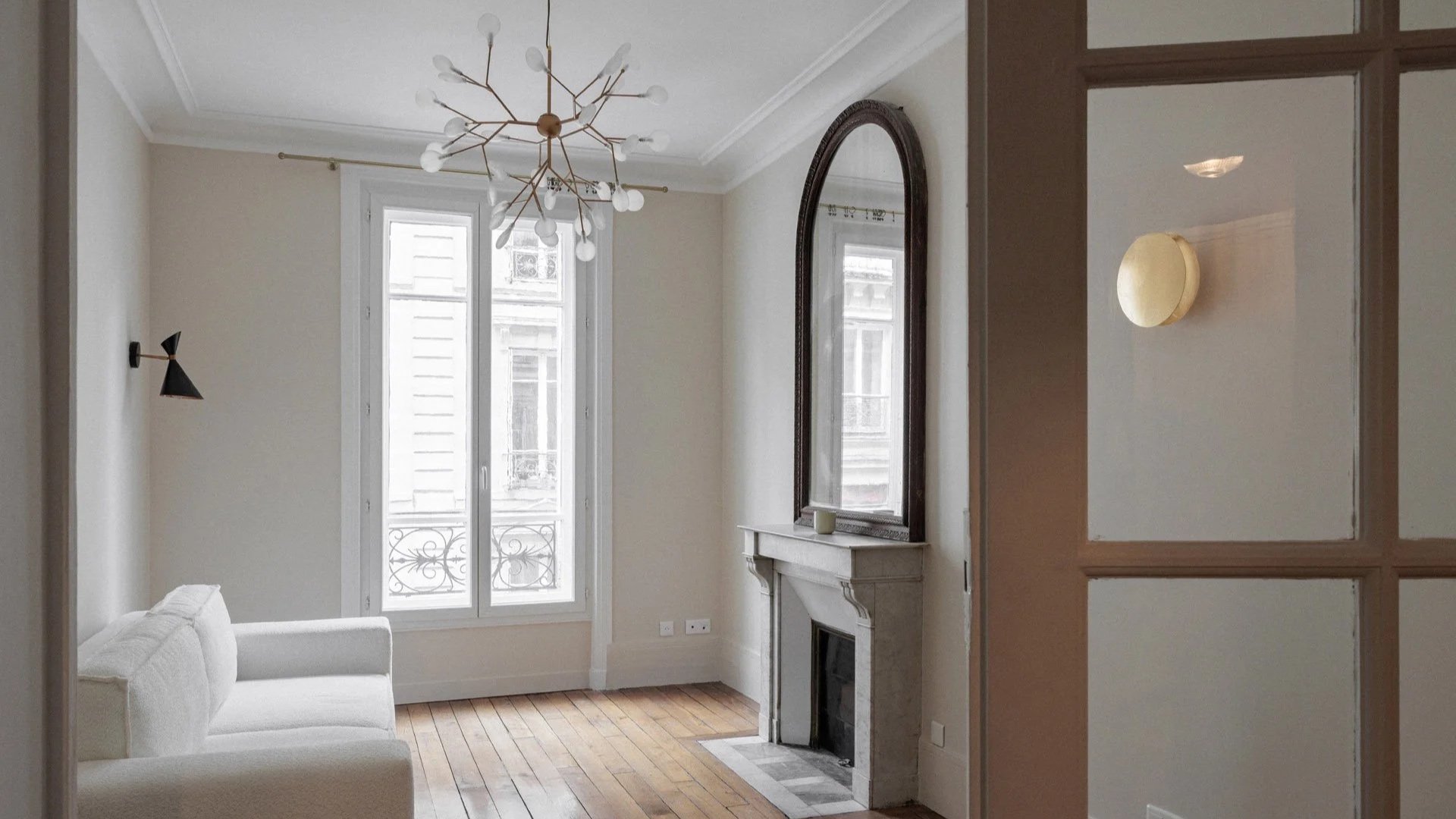 Salon d'un appartement parisien rénové par Bea Bühler — cheminée en marbre, miroir ancien, lustre contemporain