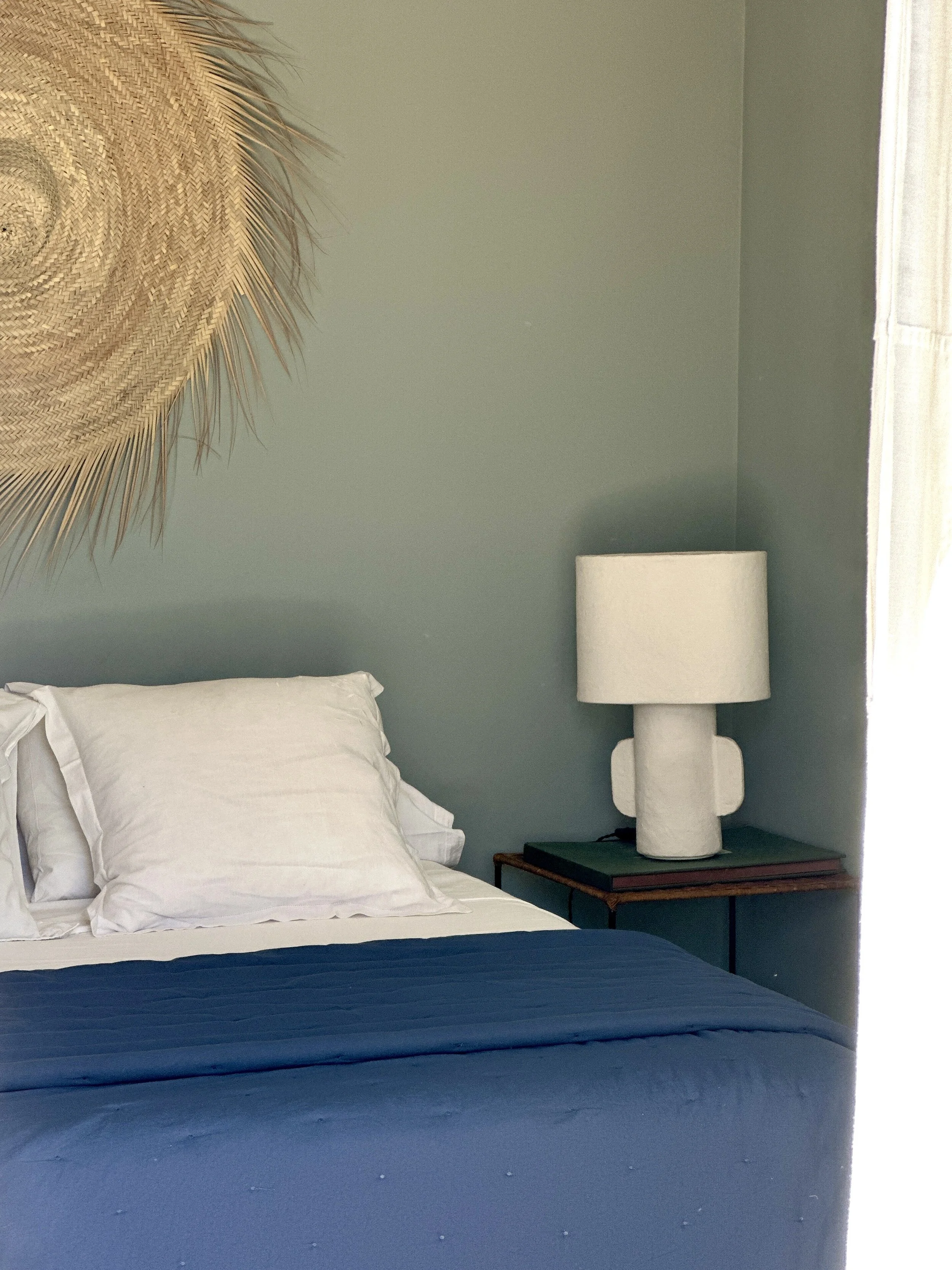 Chambre avec couvre-lit bleu, lampe de chevet blanche et suspension en fibres naturelles