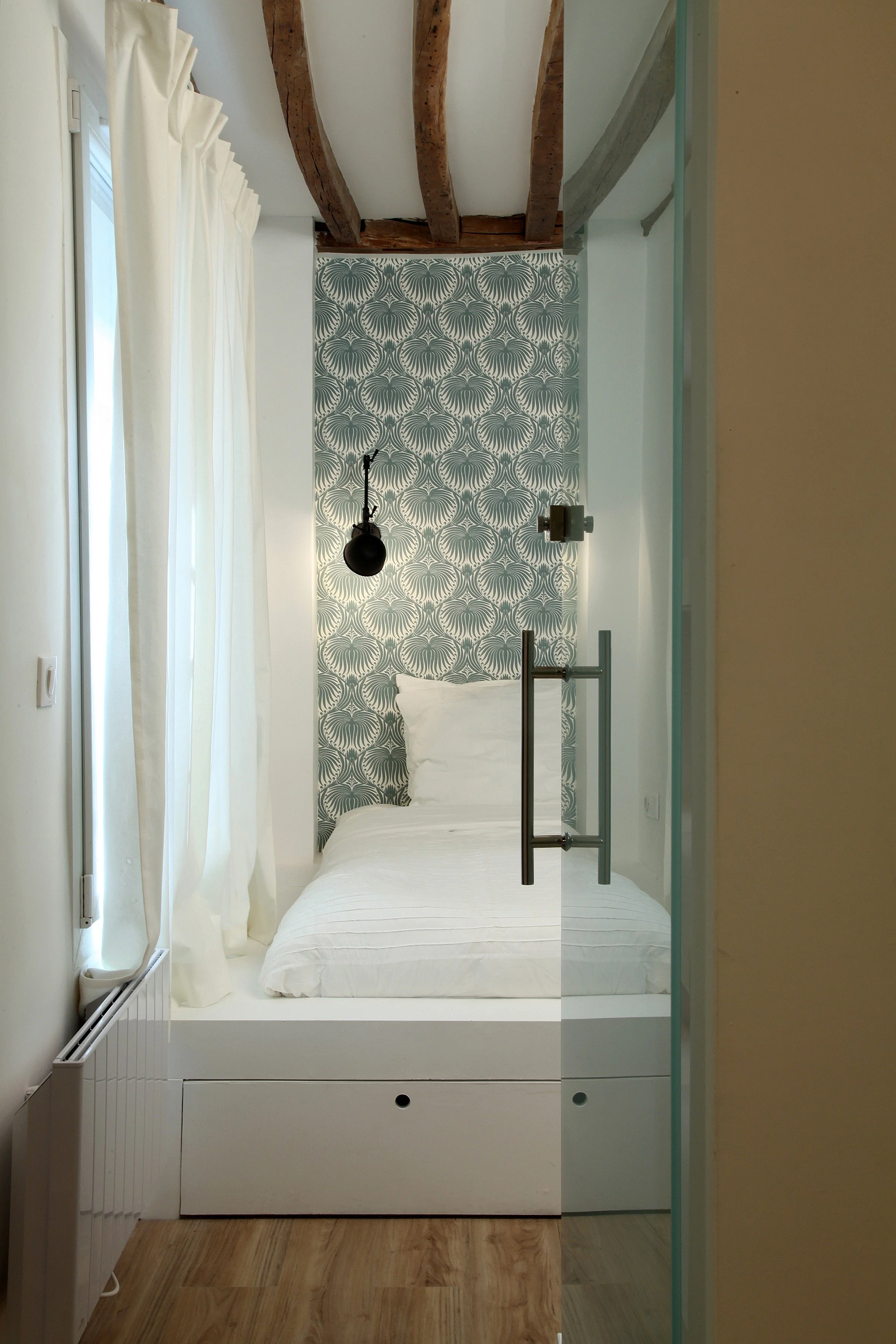 Lit sur mesure surélevé dans une alcôve tapissée de papier peint graphique Farrow & Ball, applique noire à bras articulé et poutres apparentes