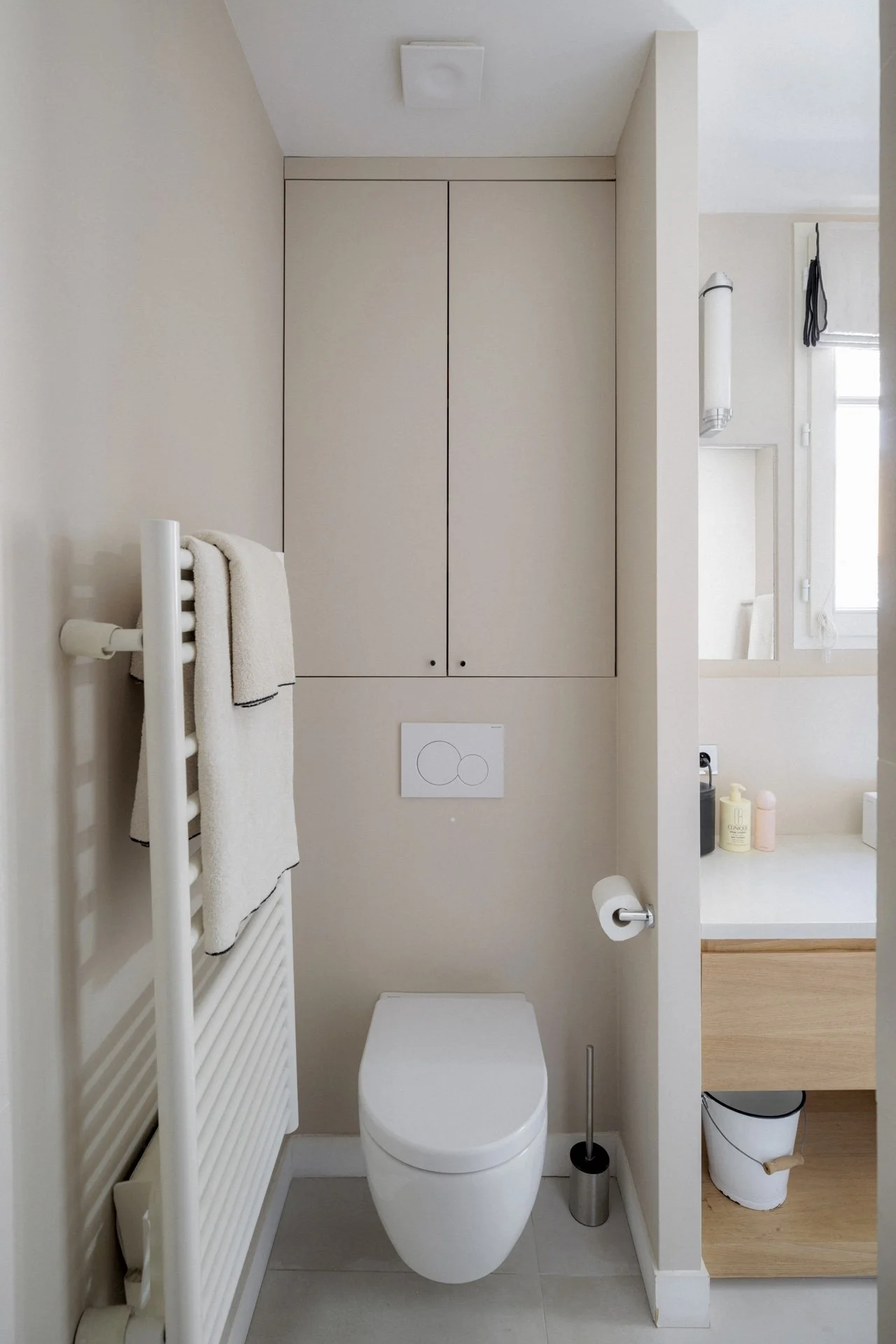 WC suspendu beige avec placard mural intégré, plaque de commande blanche et sèche-serviettes