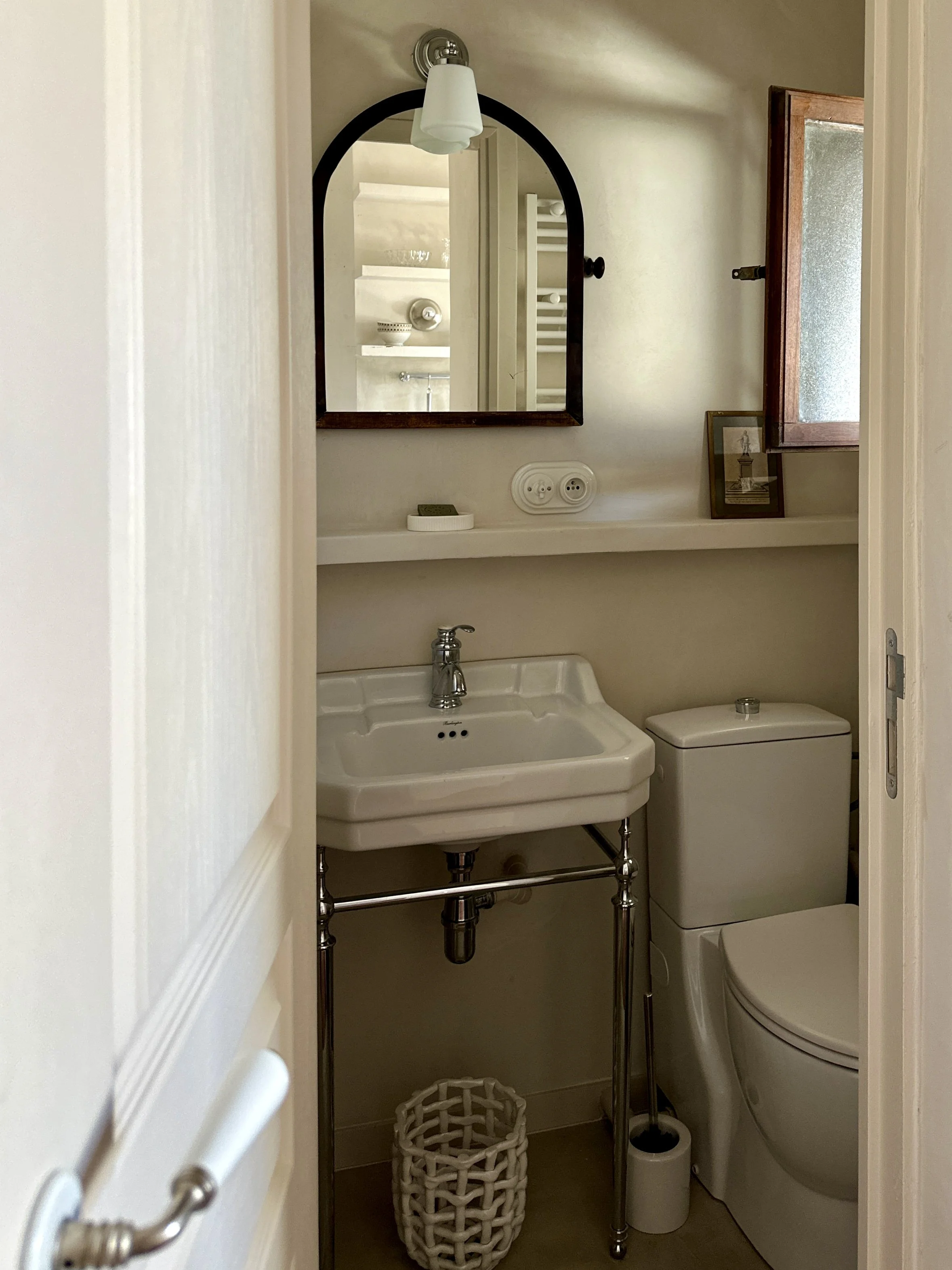 Salle d'eau en béton ciré avec fenêtre chinée, lavabo et miroir arqué