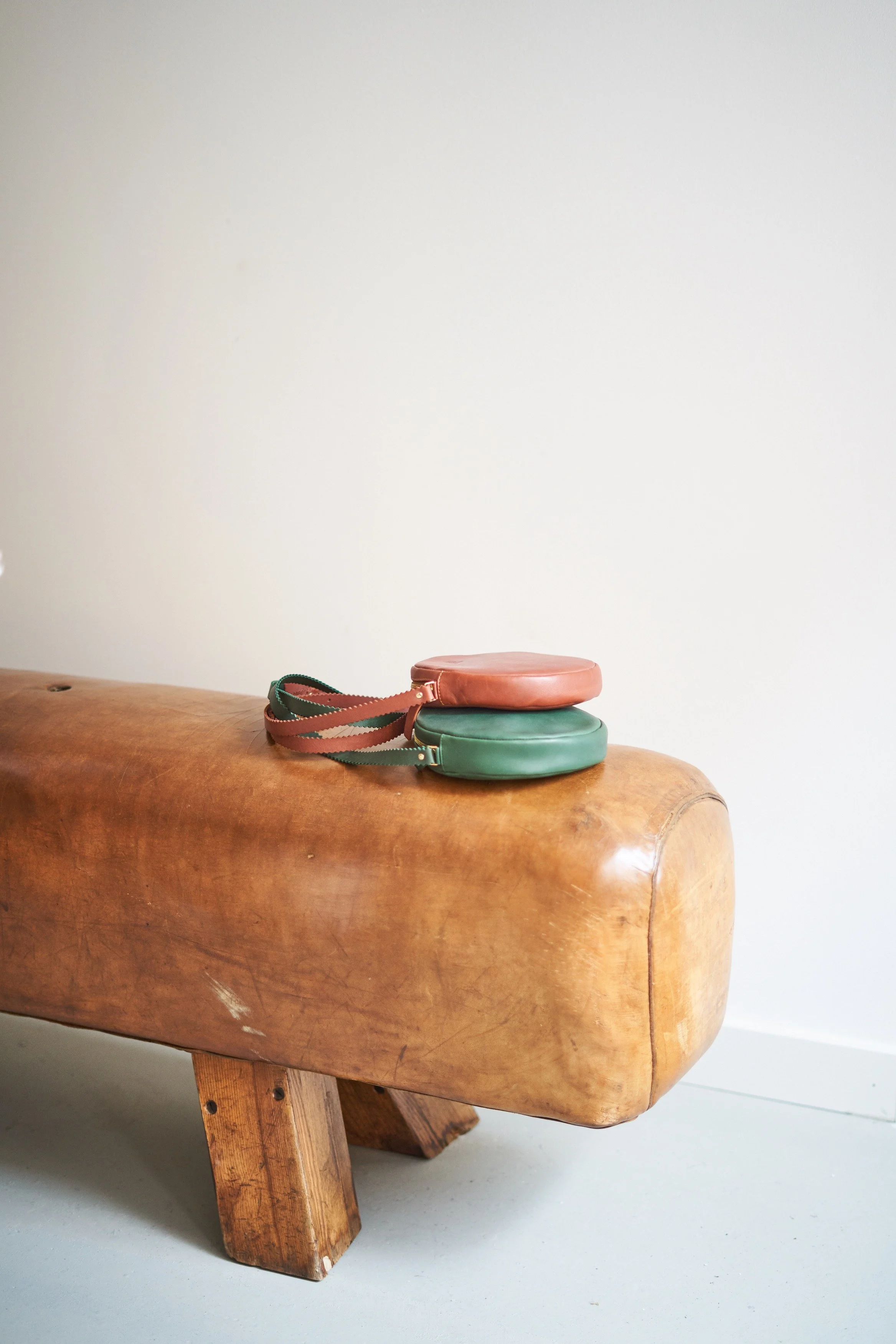 Ancien cheval d'arçons en cuir servant de banc, avec petits porte-monnaie en cuir, dans l'atelier-boutique
