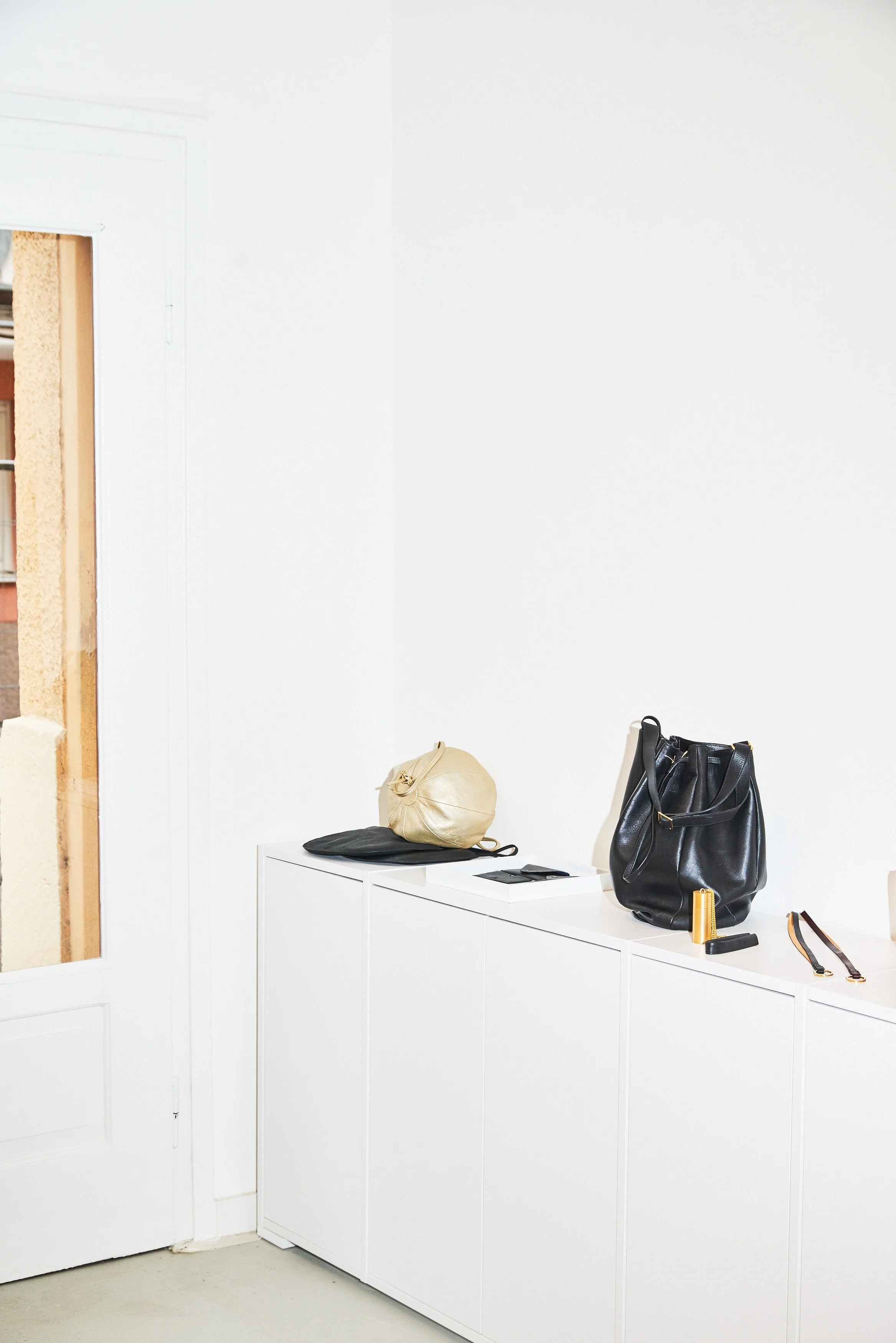 Vue de l'atelier-boutique : sac Balloon en cuir doré et sac seau en cuir noir sur les rangements intégrés, volumes épurés