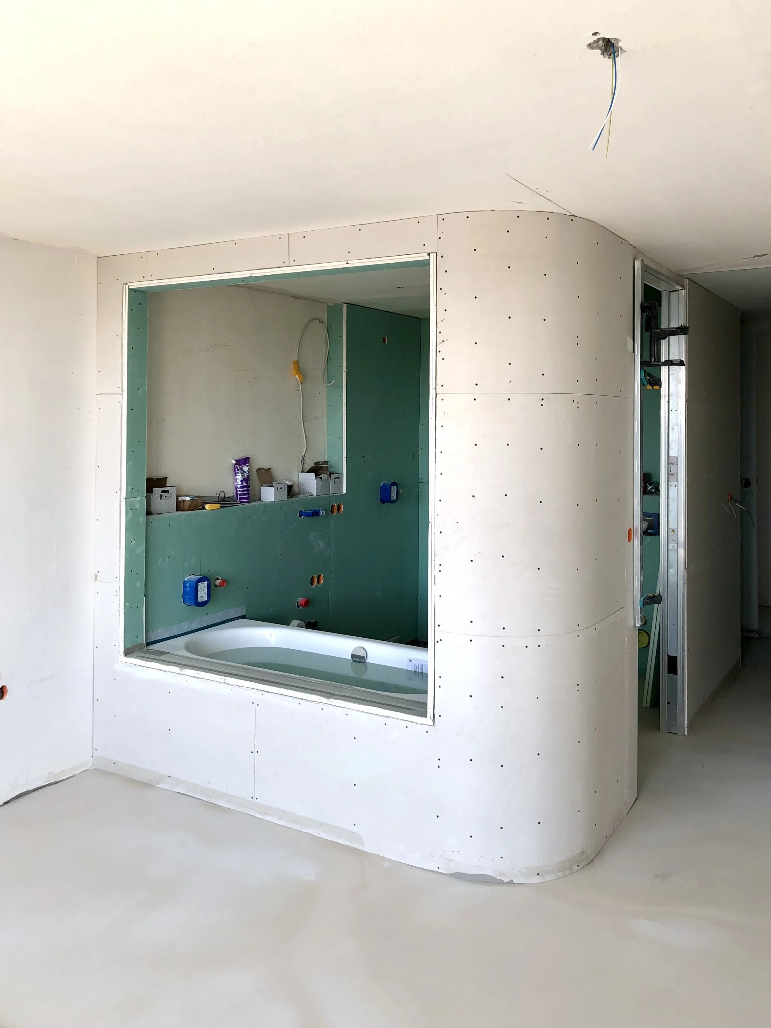 Chantier : cloison arrondie en cours de montage et grande ouverture vitrée donnant sur la baignoire de la salle de bain principale