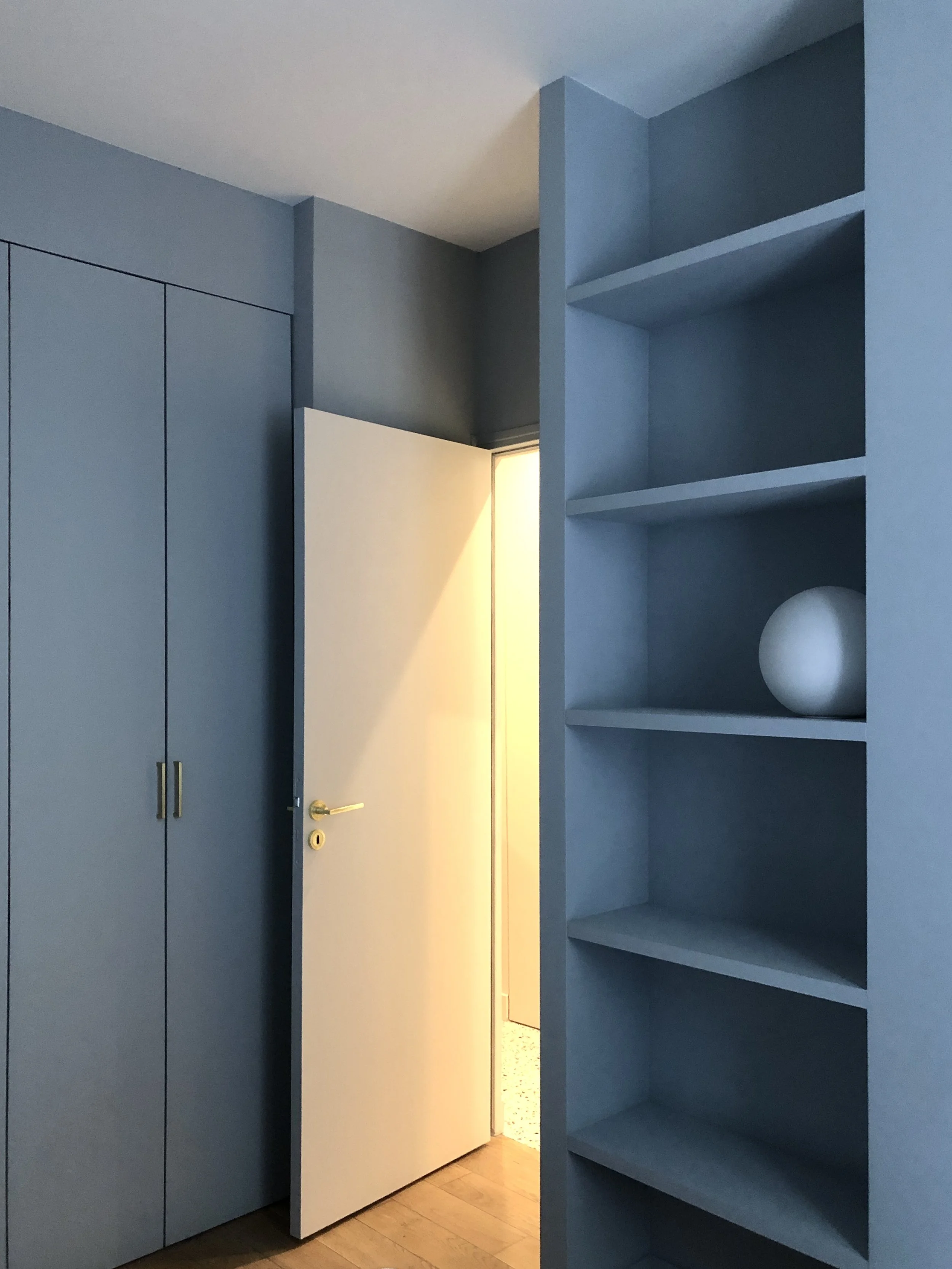Rangements sur mesure bleu-gris intégrés dans la cloison : dressing toute hauteur et bibliothèque côté chambre