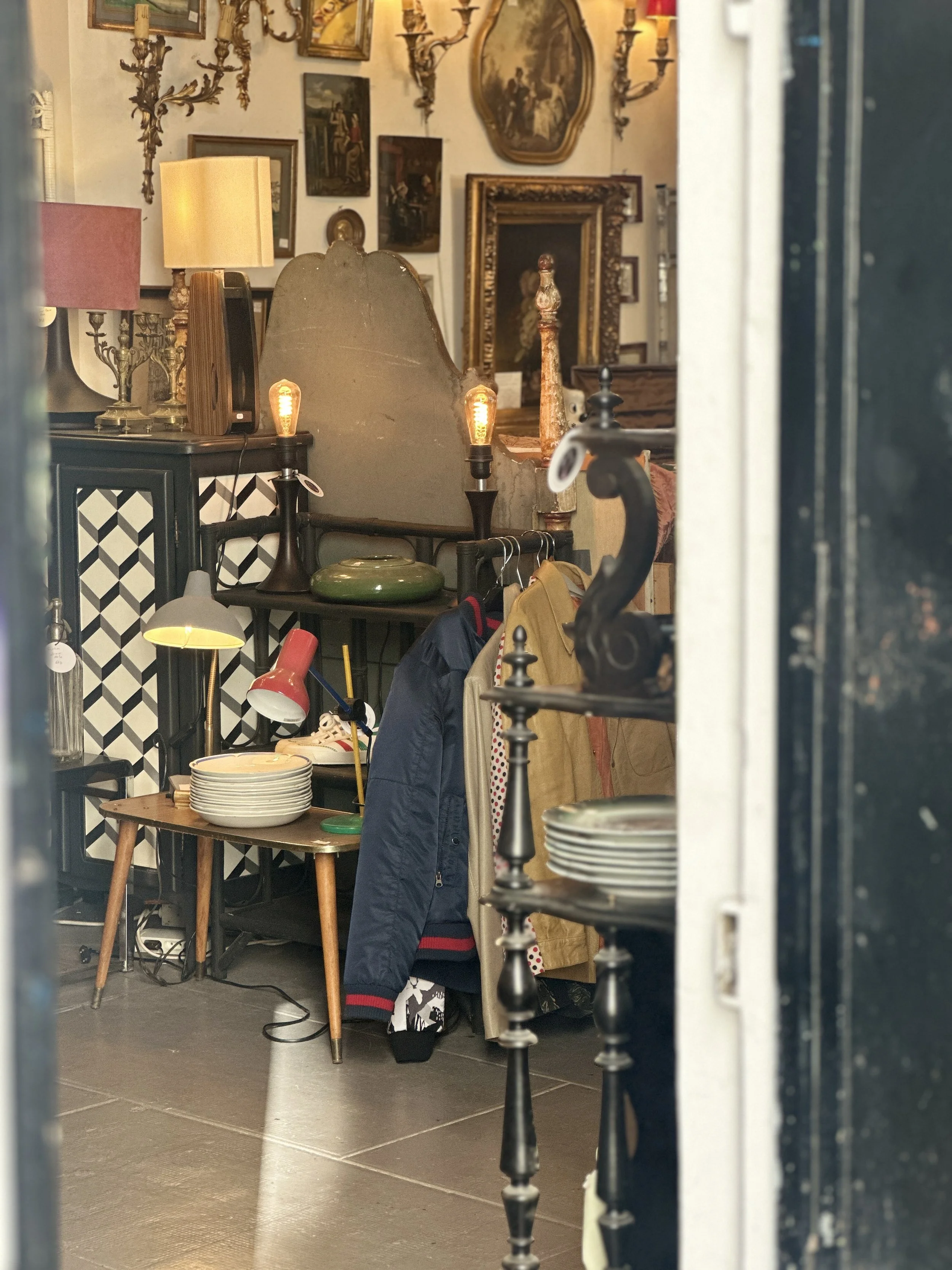 Intérieur de la brocante L'Annexe, rue du Marché Popincourt à Paris 11e : lampes anciennes, cadres dorés et pile d'assiettes blanches