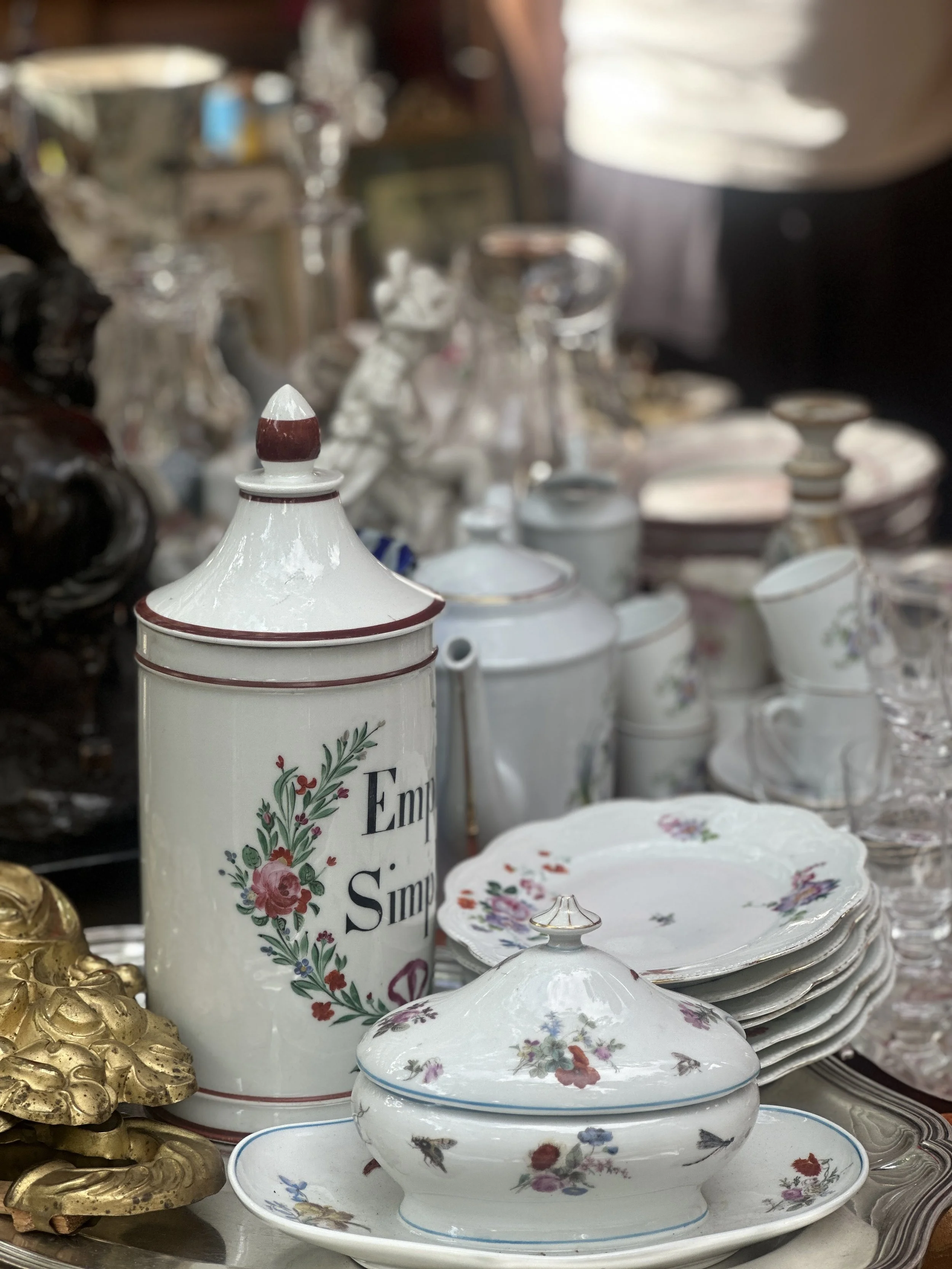 Pot d'apothicaire ancien, assiettes en porcelaine à fleurs et soupière sur un plateau en argent, aux Puces de Vanves à Paris