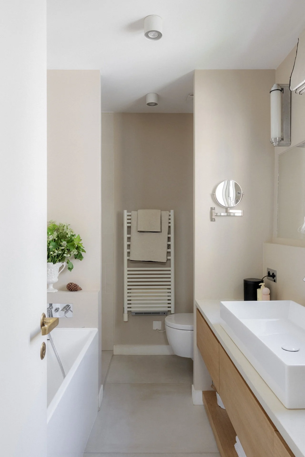 Vue d'ensemble de la salle de bain beige avec baignoire, sèche-serviettes blanc, WC suspendu et meuble vasque en bois