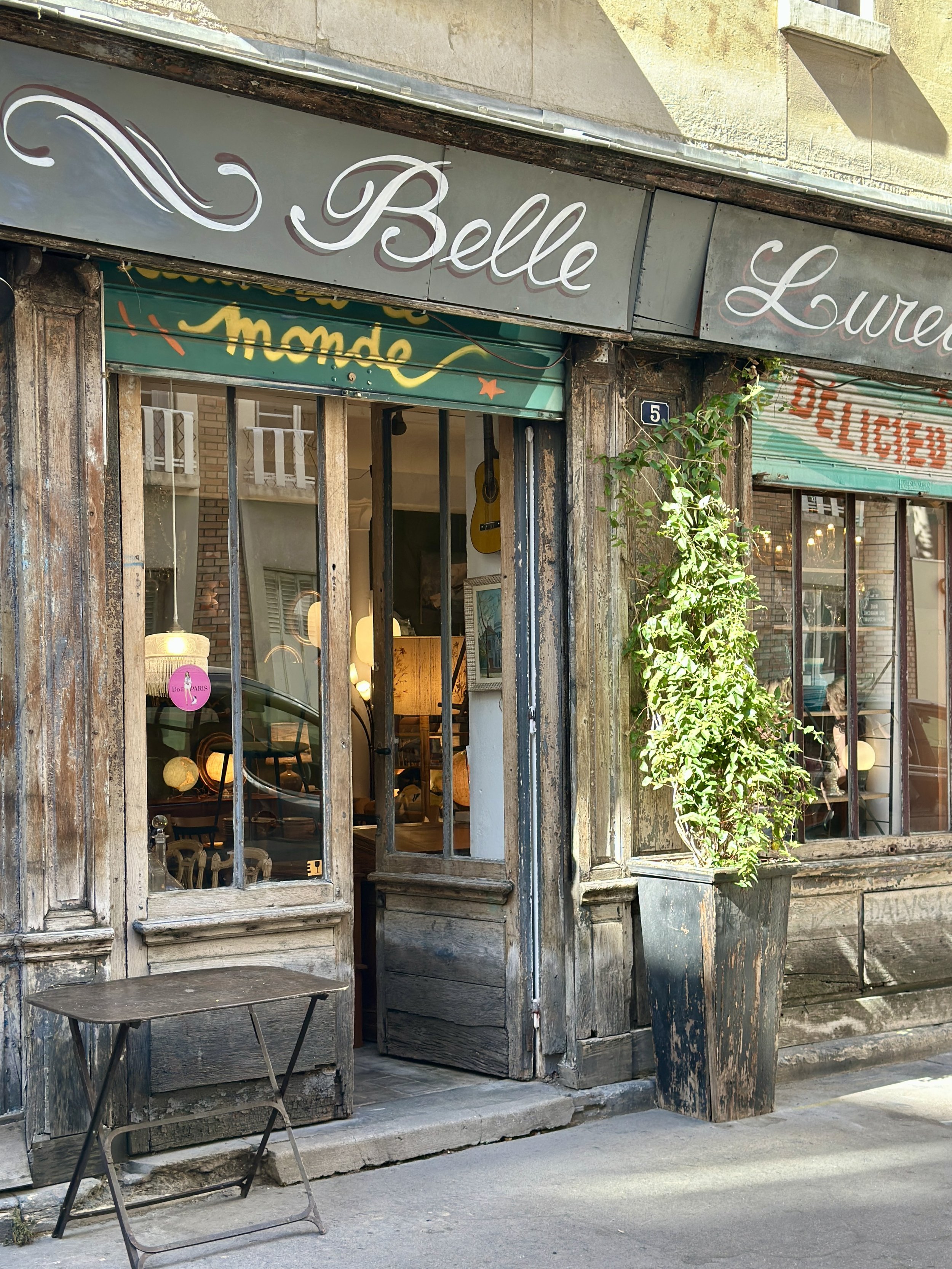 Intérieur de la brocante Belle Lurette à Paris : cadres dorés, lampes anciennes et pile d'assiettes blanches