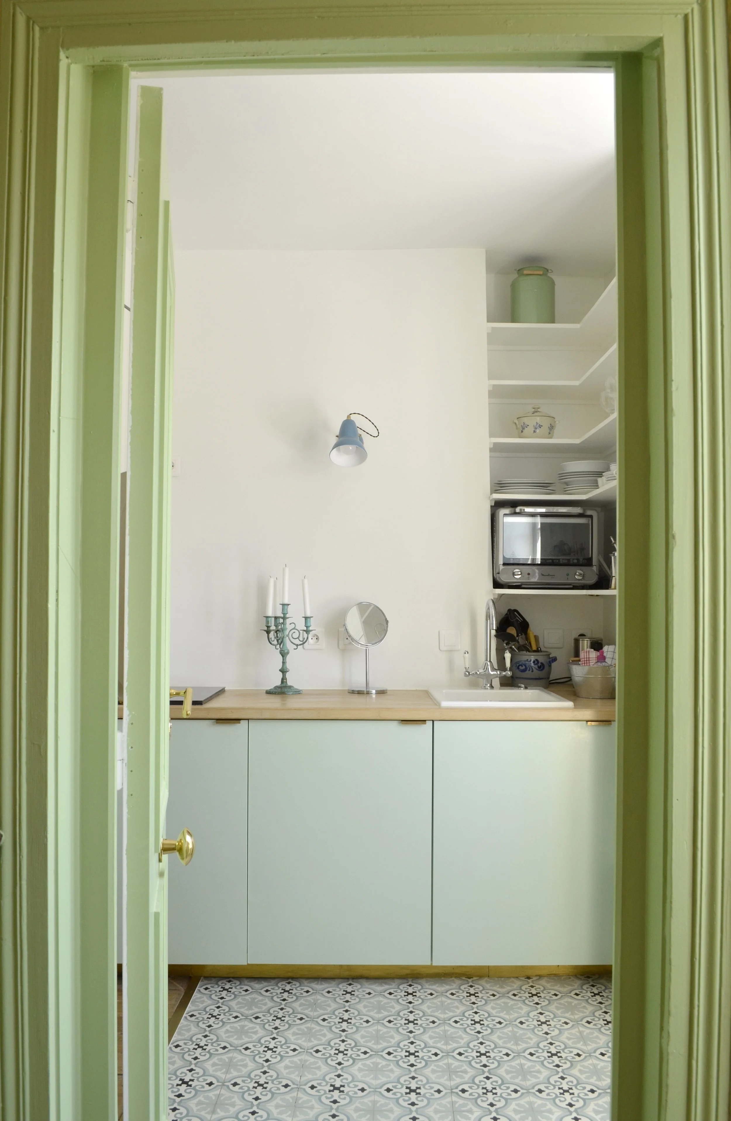 Entrée du studio avec porte peinte en vert amande ouvrant sur la kitchenette vert d'eau et le sol en carreaux de ciment