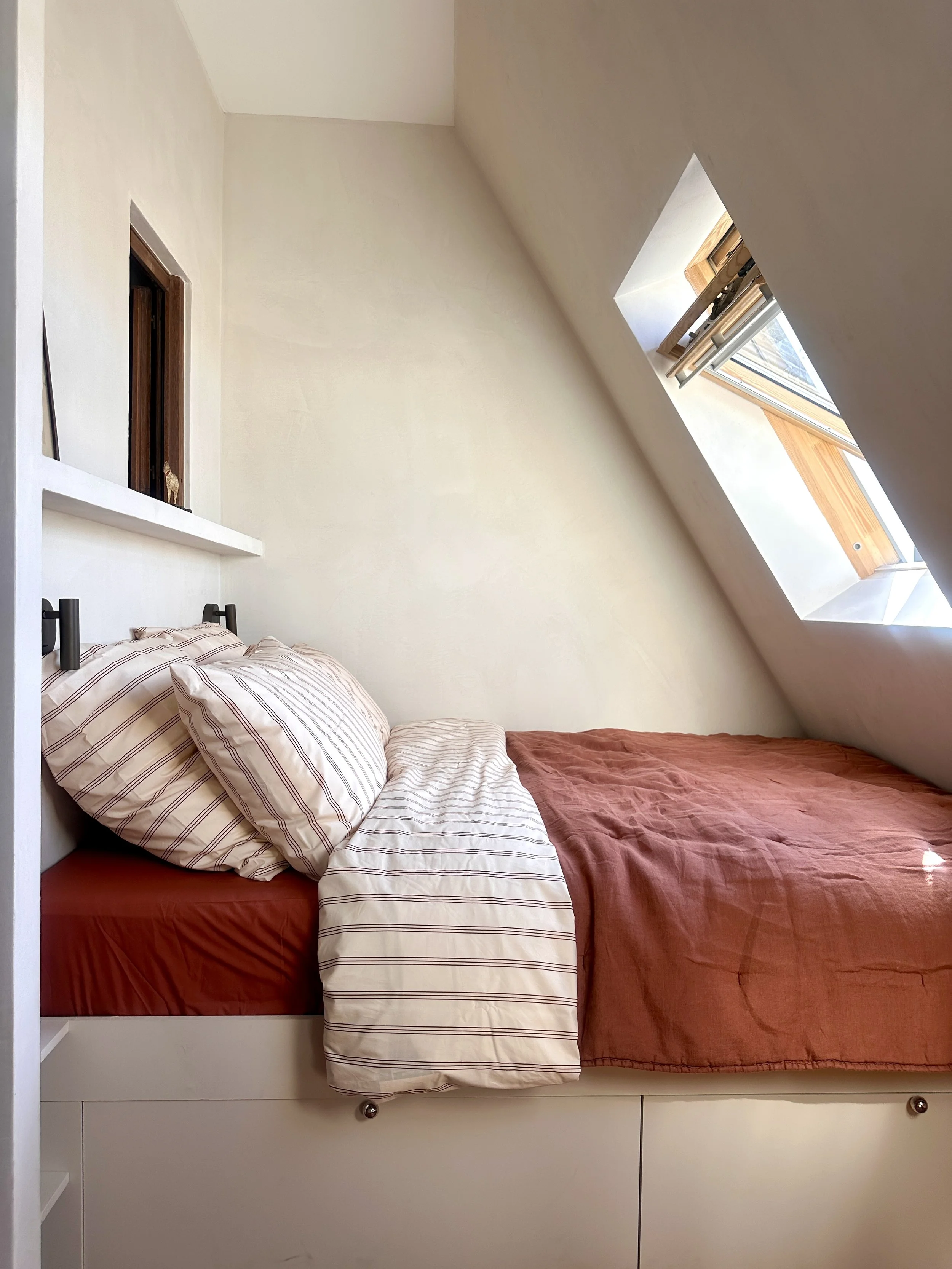 Lit sous rampant éclairé par la fenêtre de toit, studio mansardé rénové à Paris