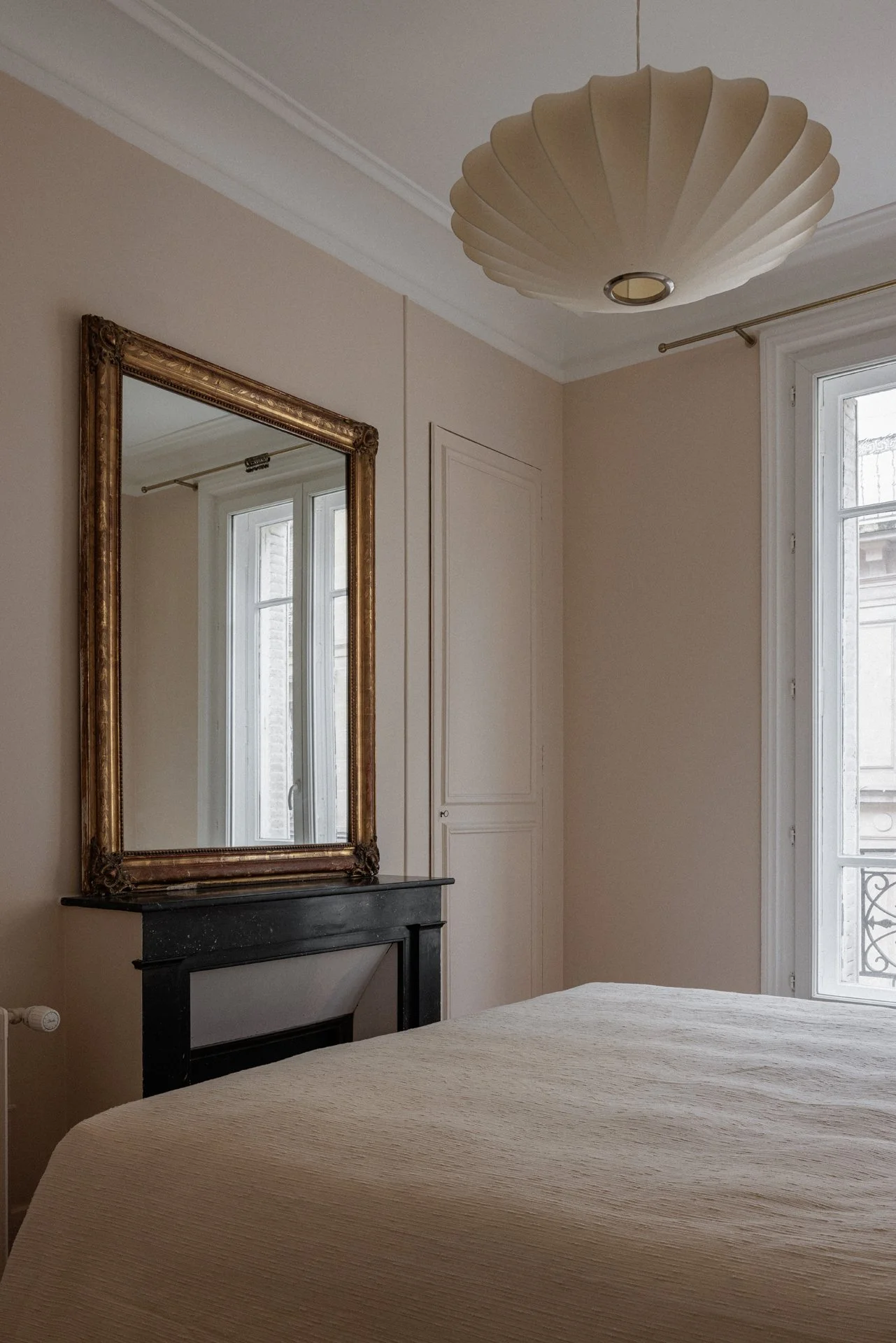 Chambre d'un appartement haussmannien rénové par Bea Bühler : cheminée en marbre noir, miroir doré chiné et suspension contemporaine.