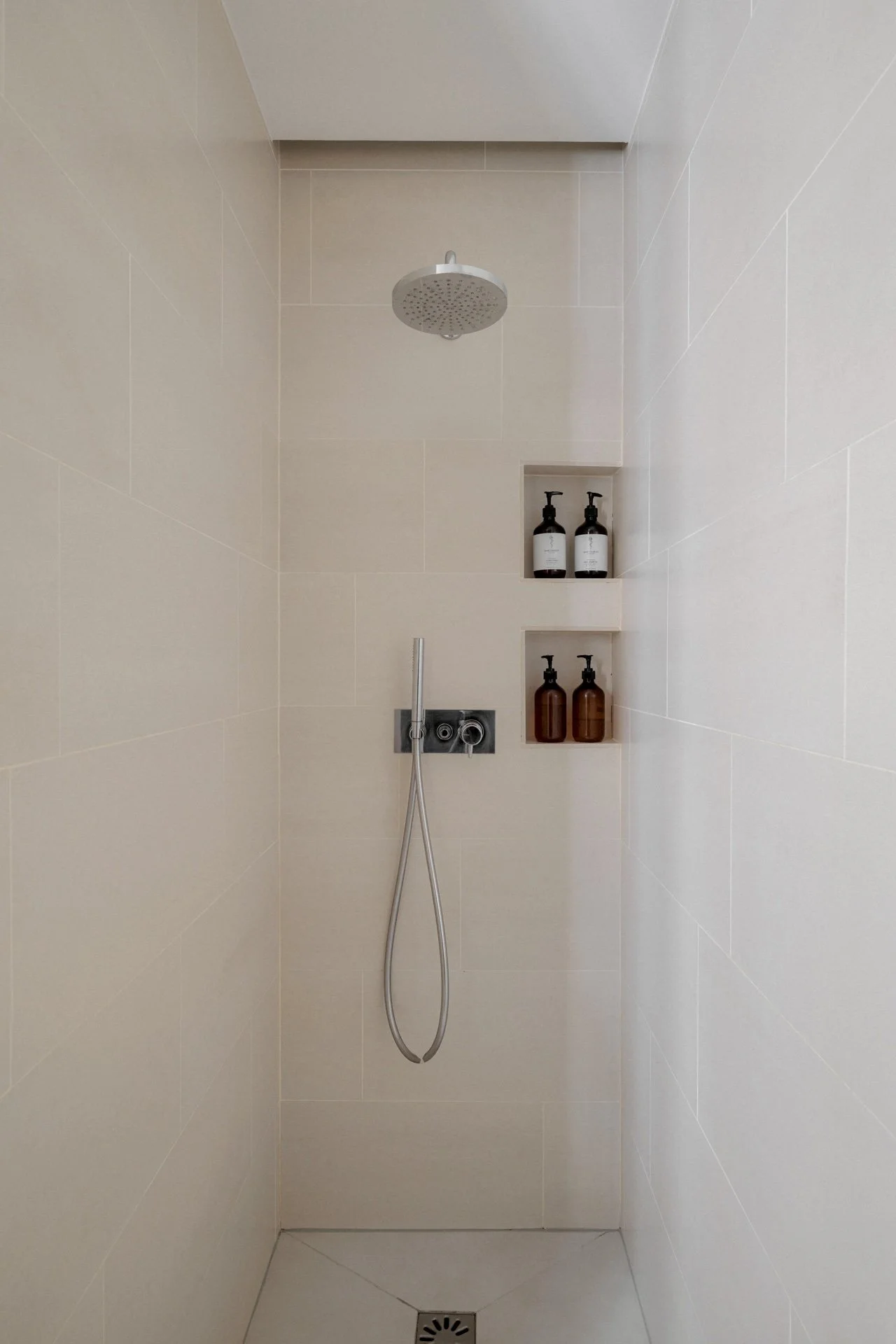 Douche à l'italienne avec carrelage beige, pommeau de douche pluie, douchette chromée et deux niches murales