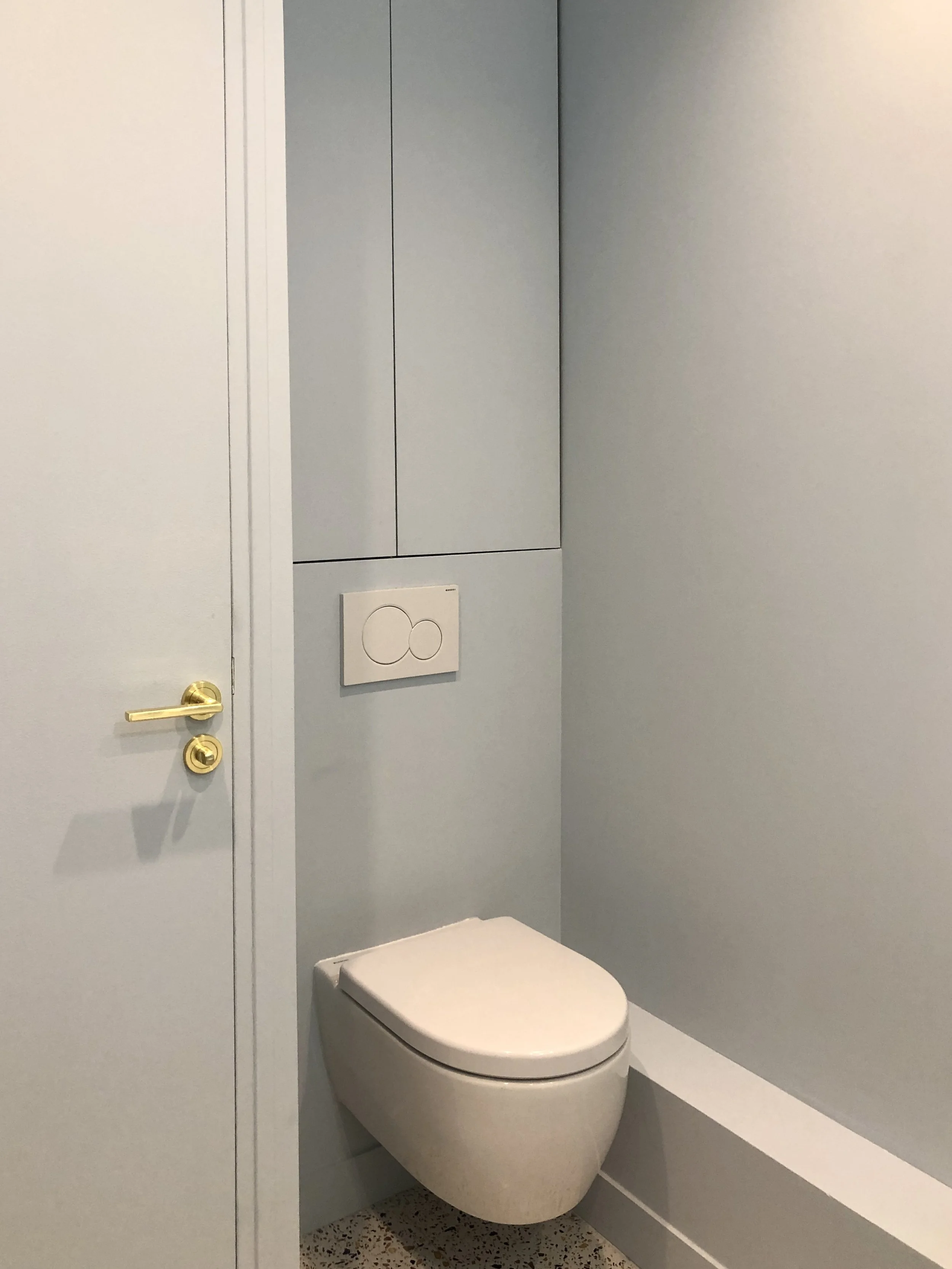 WC suspendu avec plaque de chasse encastrée, poignée de porte en laiton et sol en terrazzo