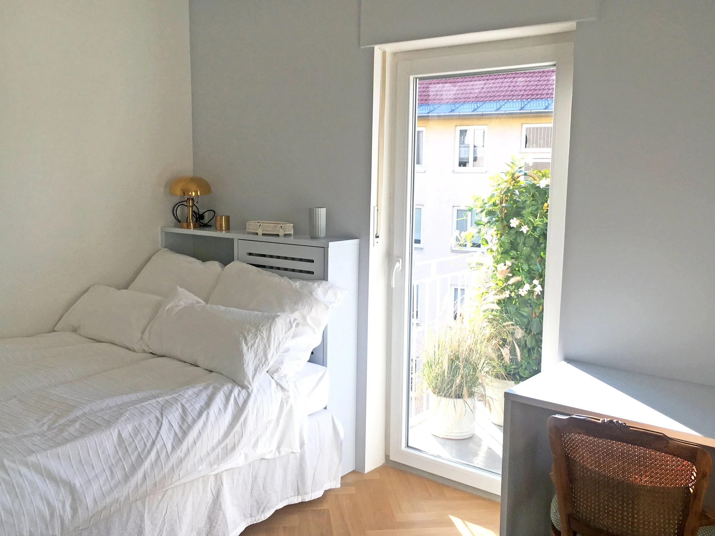 Chambre avec tête de lit et rangements dessinés sur mesure, ouverte sur la fenêtre et le balcon