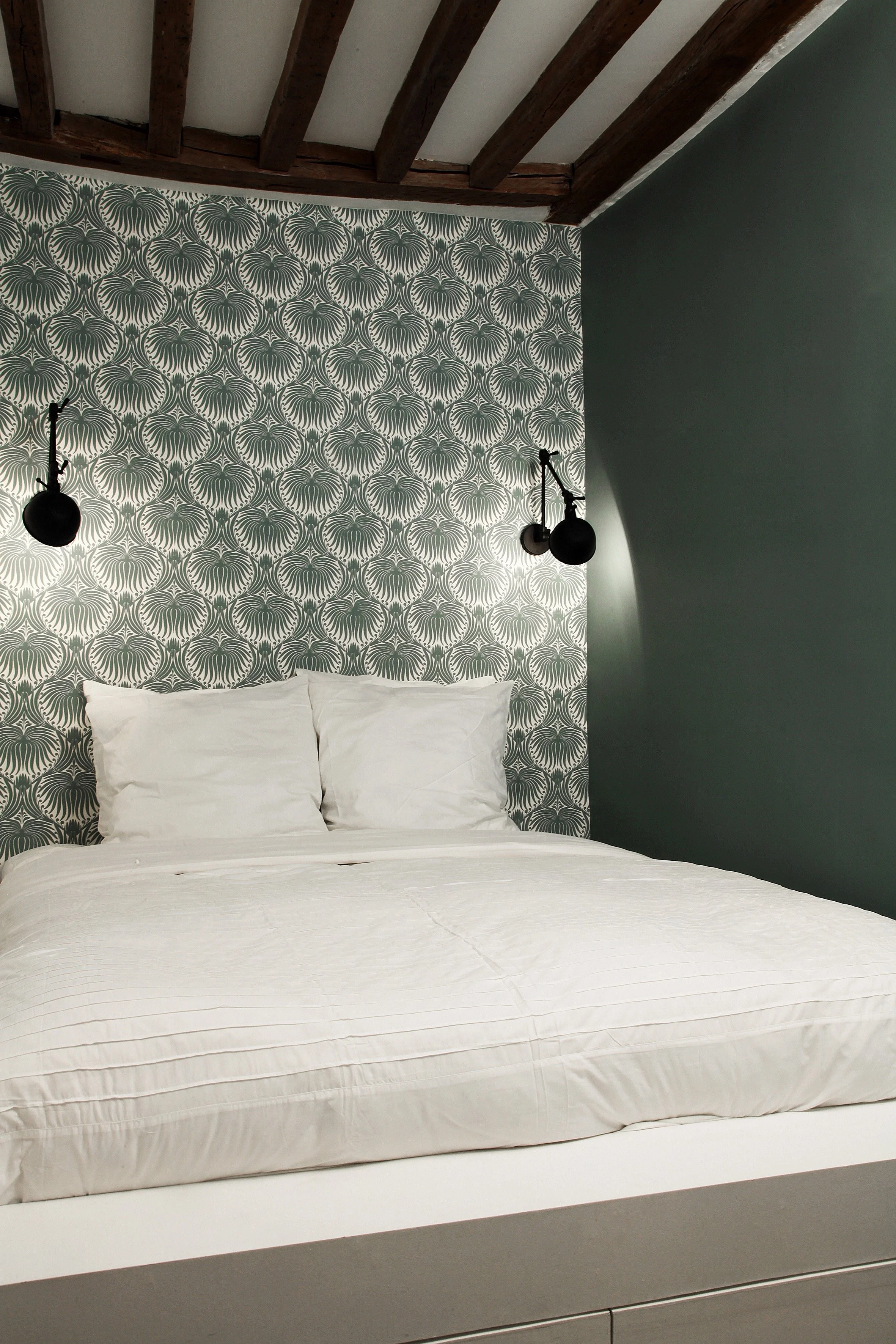 Chambre avec lit sur mesure, papier peint graphique Farrow & Ball, mur vert profond et deux appliques chinées à bras articulés noirs