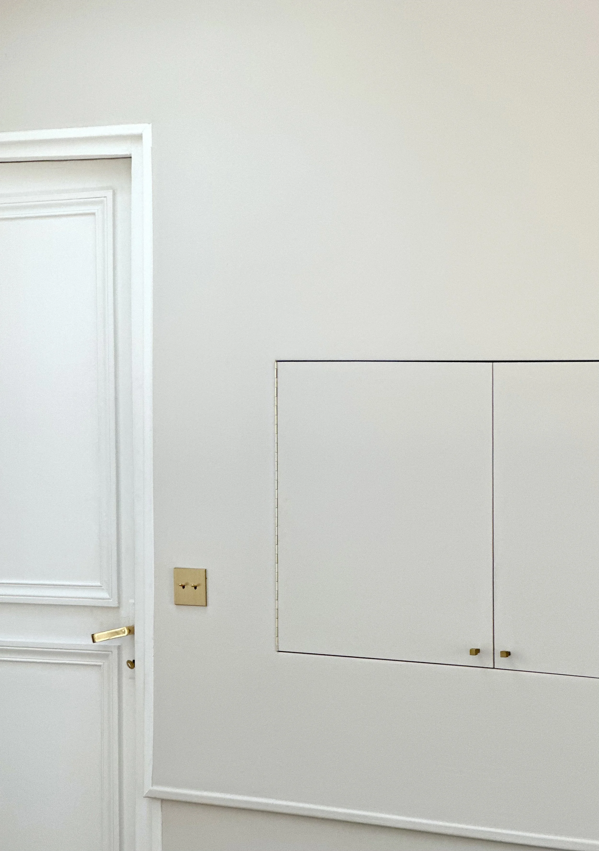 Télévision dissimulée derrière un placard mural affleurant, à côté d'une porte à double battant d'origine