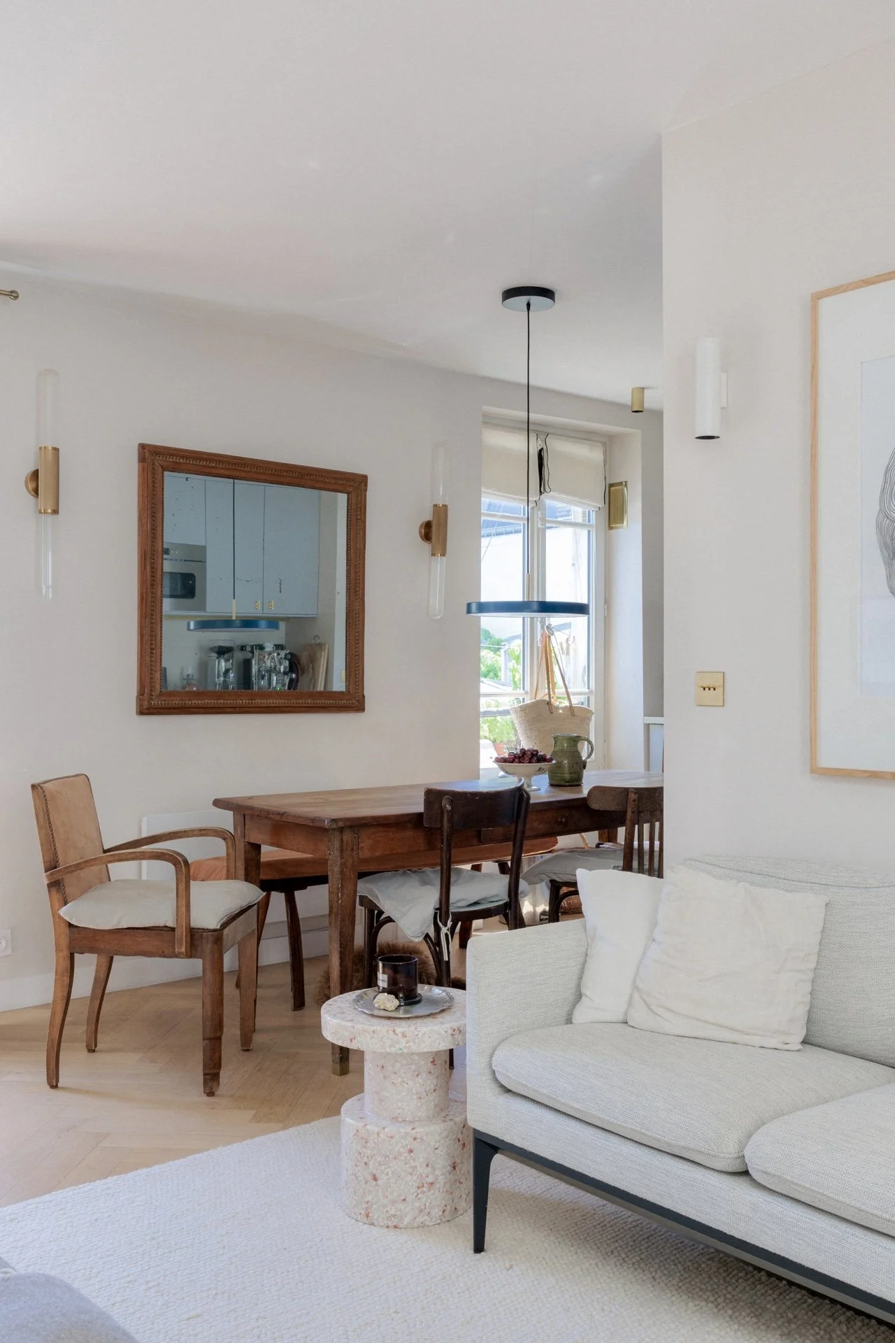 Salon et salle à manger avec table en bois vintage, chaises anciennes, miroir en bois sculpté, canapé beige et suspension bleue au-dessus de la table