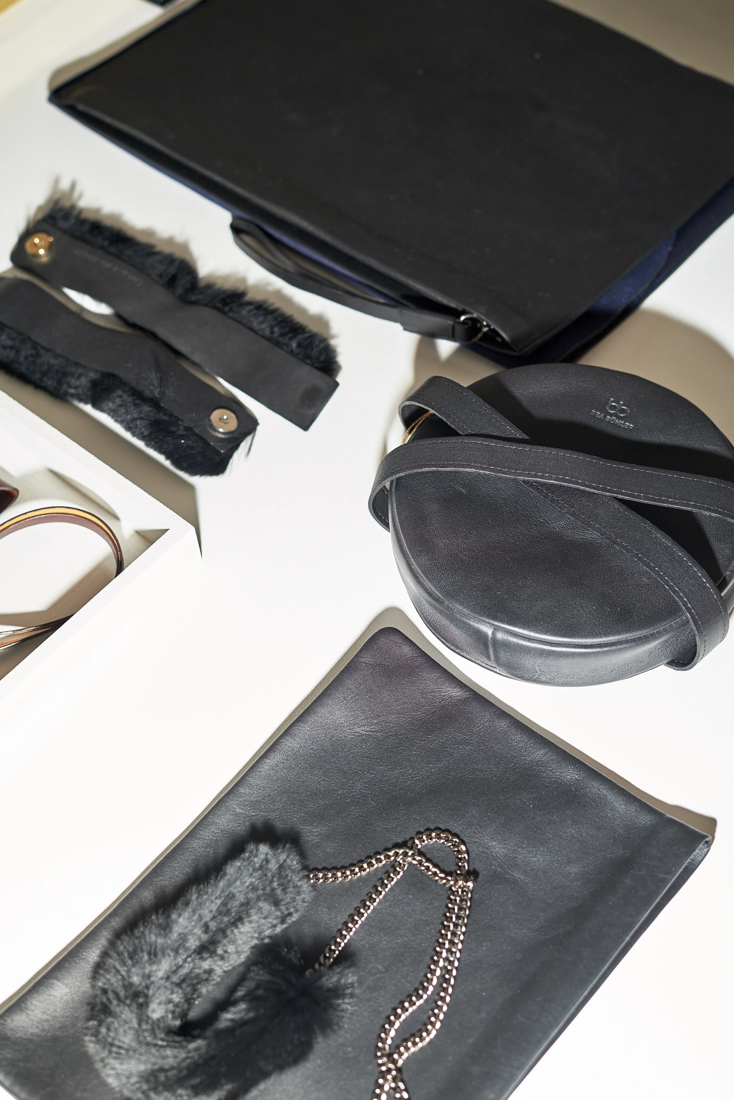 Maroquinerie en cuir noir vue du dessus : pochettes, sac rond et ceintures de la ligne Bea Bühler