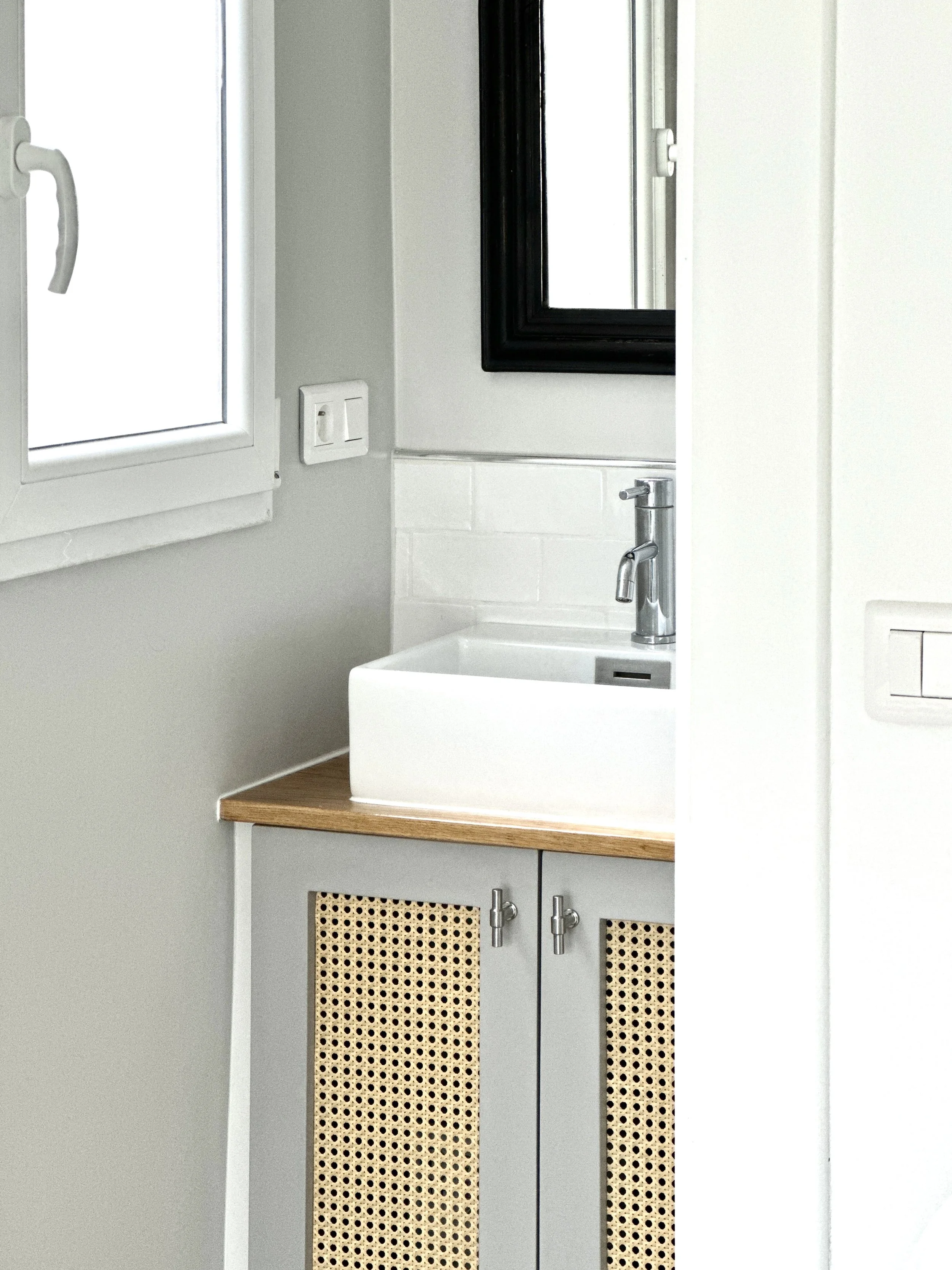 Salle de bains compacte avec meuble vasque sur mesure à portes cannées, plan en bois et miroir noir