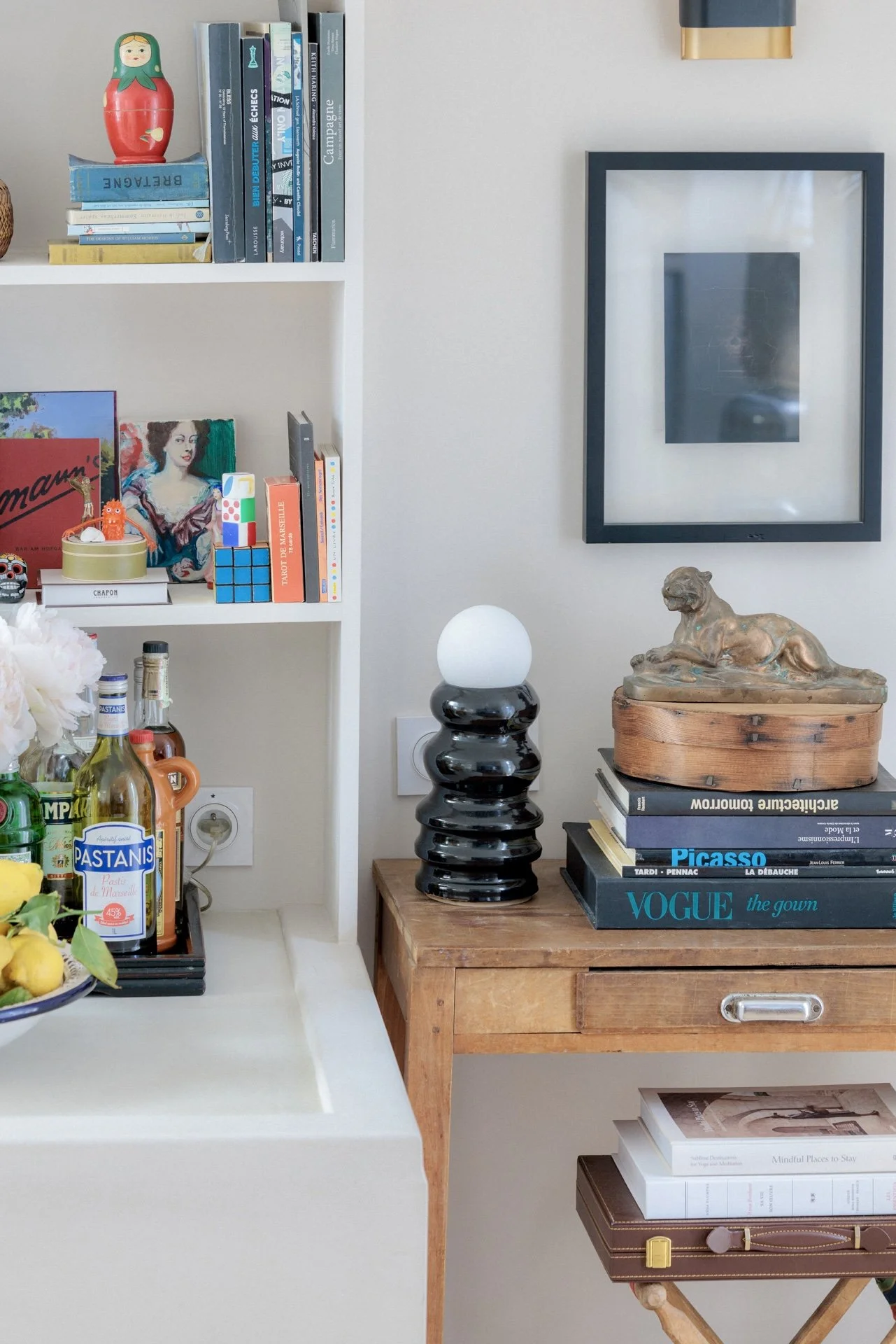 Console en bois ancien avec lampe boule noire, pile de livres, statuette de lion en bronze et bibliothèque avec objets décoratifs et bar à liqueurs