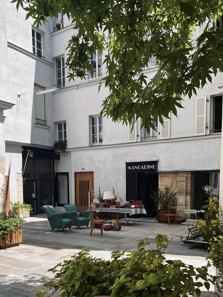 Cour du Village Saint-Paul dans le Marais : fauteuils vintage verts, lampes et objets chinés devant les boutiques d'antiquaires