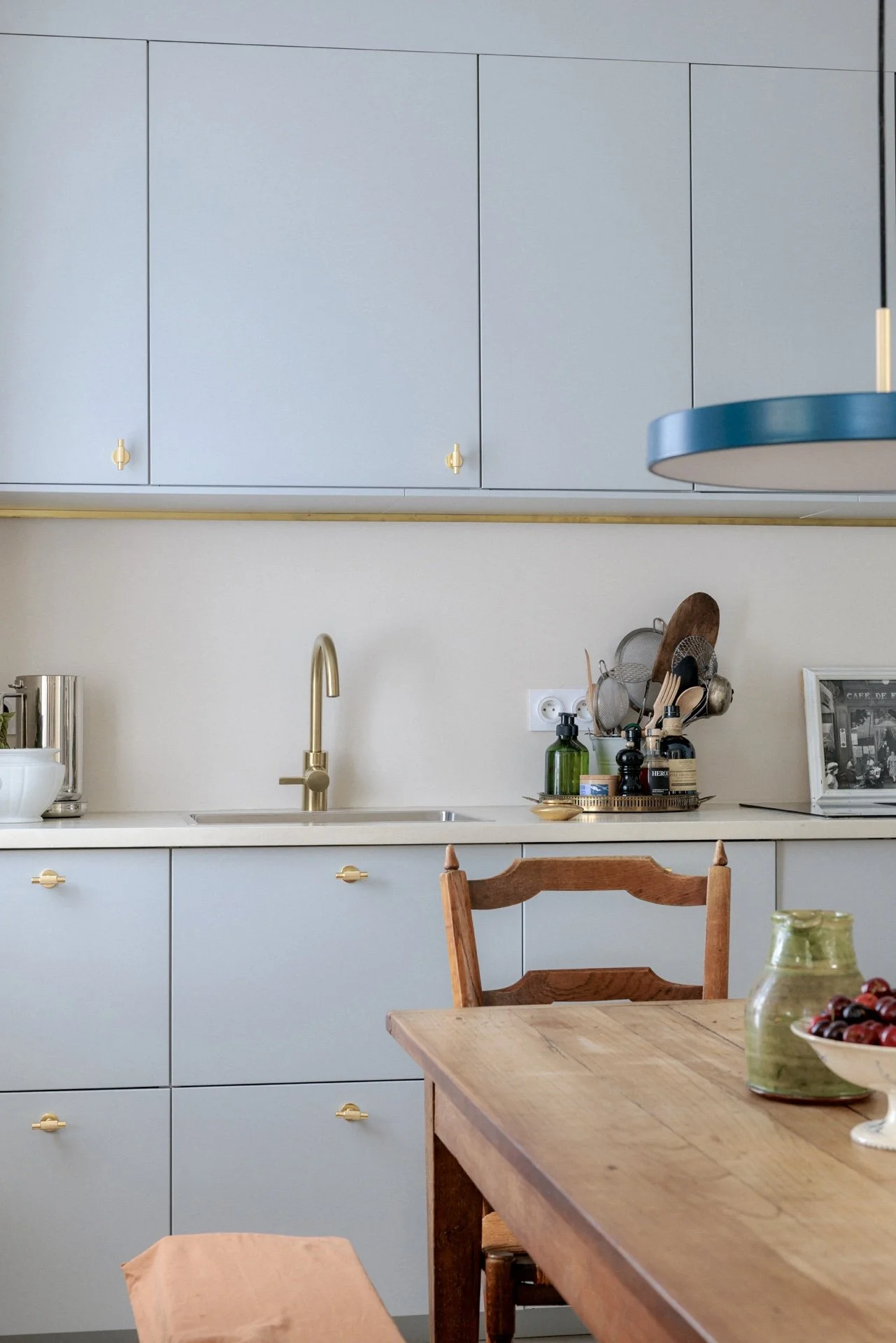 Cuisine bleu gris avec façades et poignées laiton, robinet doré, égouttoir à couverts et table en bois ancien avec chaise vintage