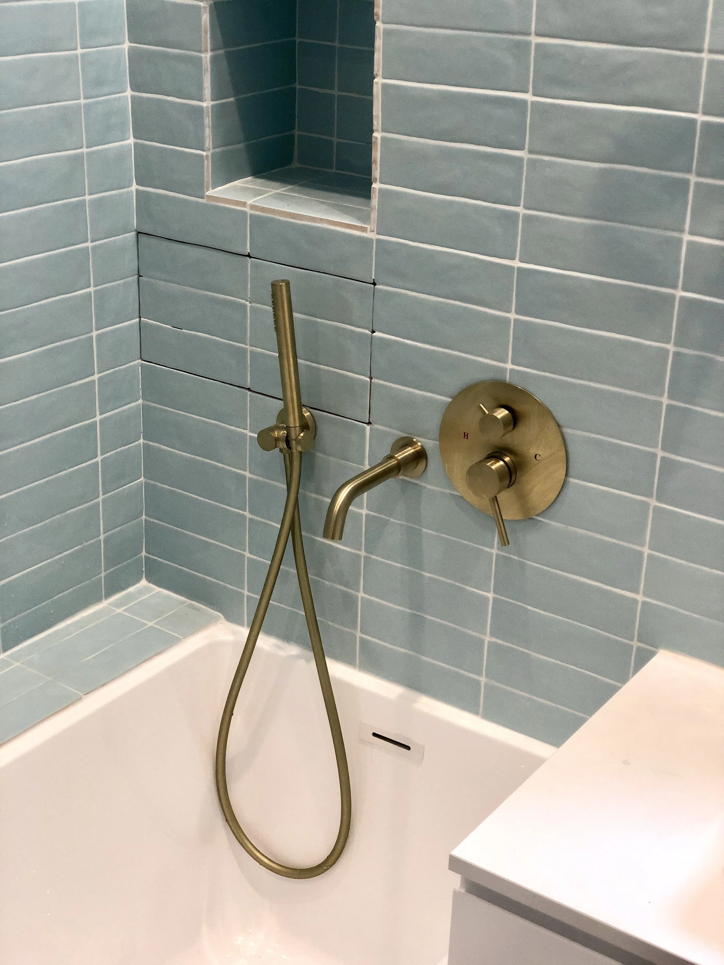 Salle de bains carrelée vert d'eau avec baignoire, niche intégrée et robinetterie en laiton brossé