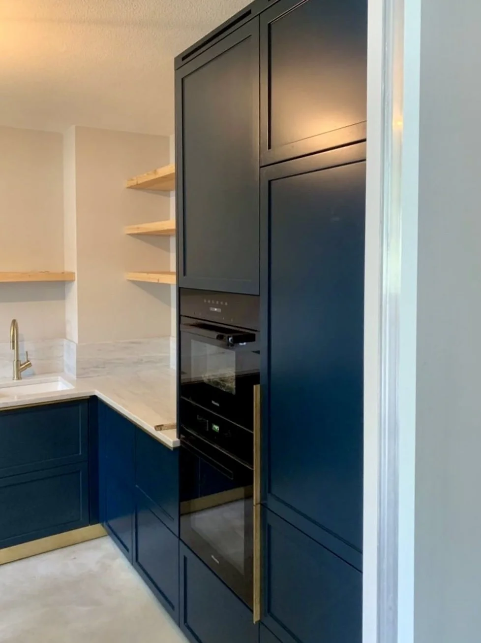 Cuisine sur mesure bleu marine avec plan de travail en marbre mat, poignées et plinthes en laiton, sol en béton ciré, rénovation d'une maison à Bogenhausen, Munich