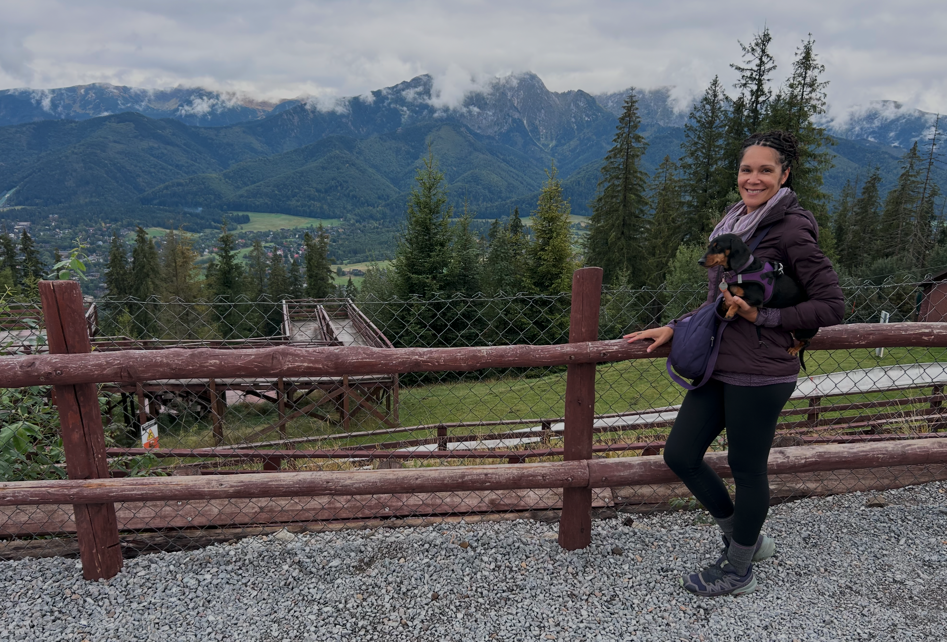 Dr. Anya Szigeti holding her miniature dachshund Mylo with cloud covered Tatra Mountains near Zakopane, Poland, in the background.