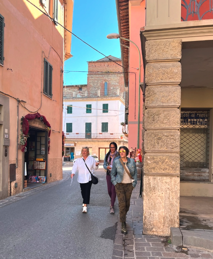 Three women walking along a narrow street lined with pastel buildings in Terricciola, Tuscany.