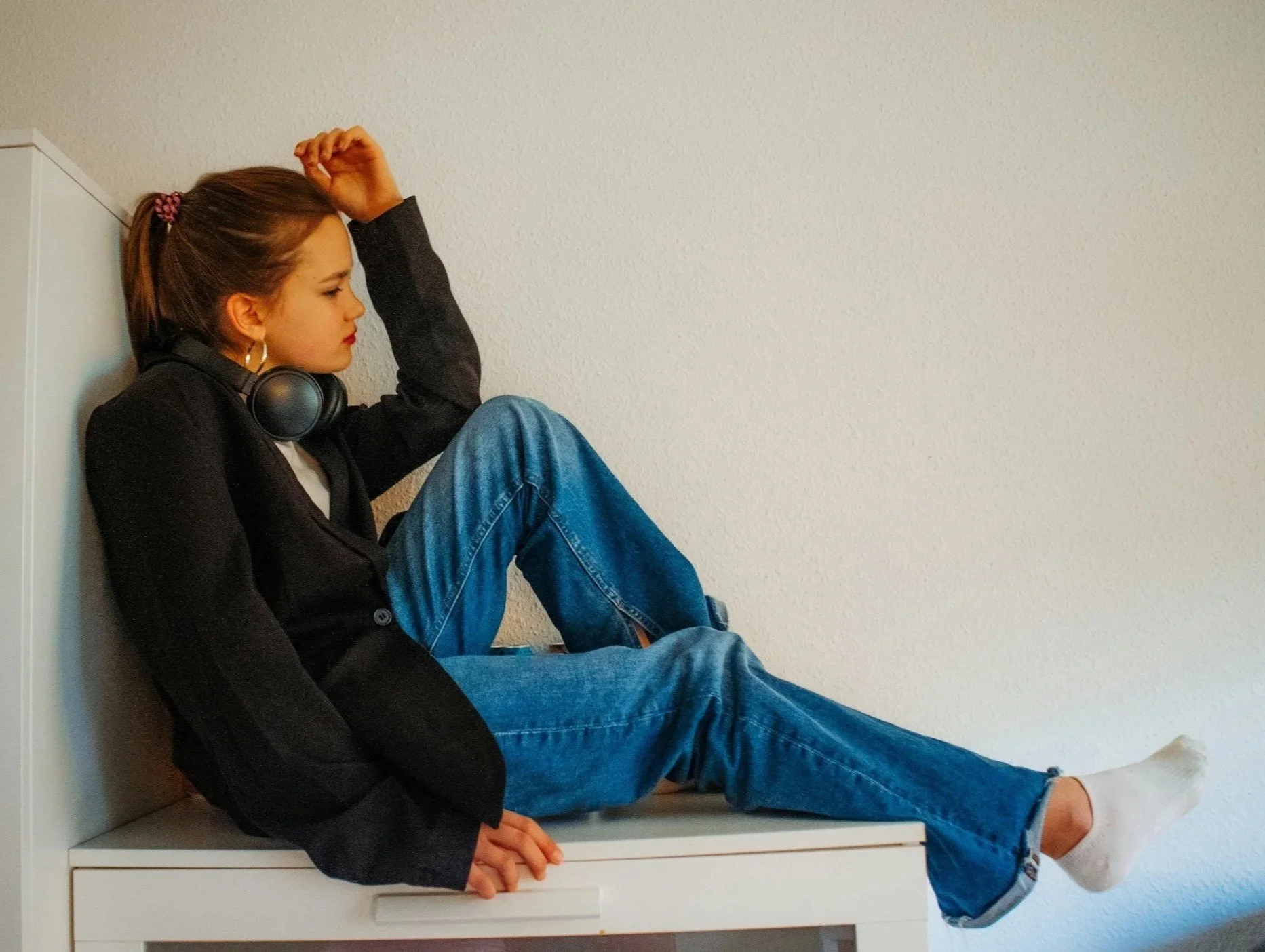 Teenager sitting on a white dresser with her back against a wall, looking overwhelmed and upset.