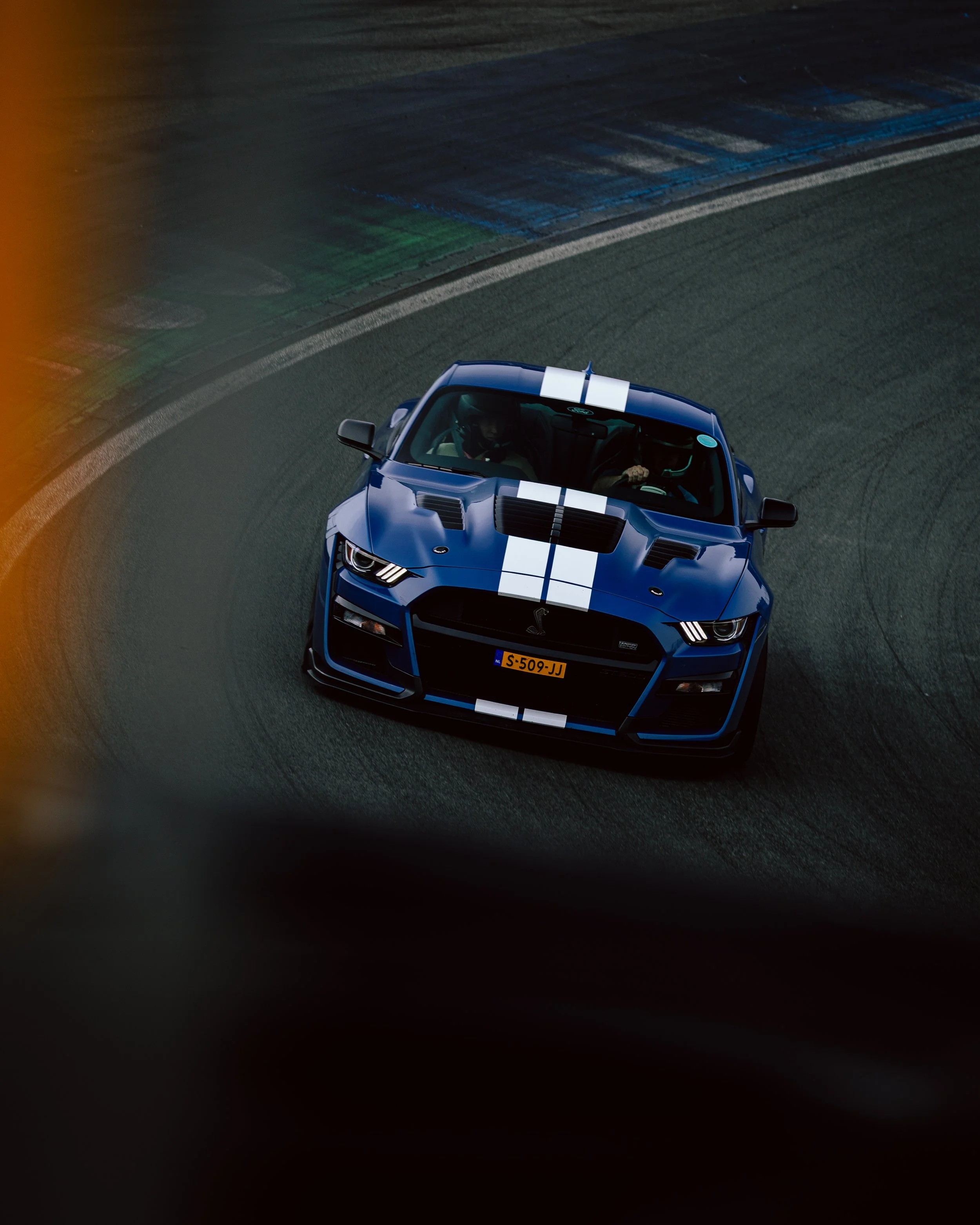 A blue sports car with white racing stripes navigating a race track turn.