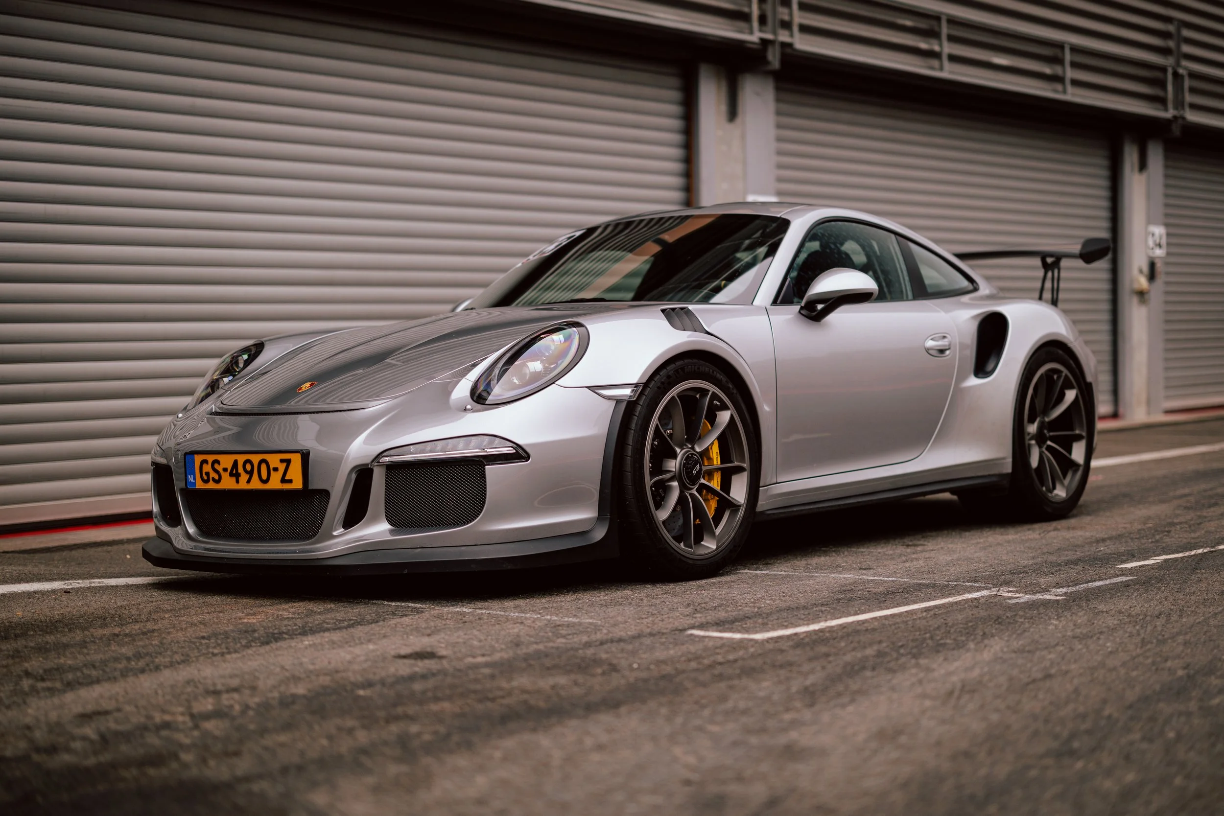 Silver Porsche 911 sports car parked in front of garage doors.