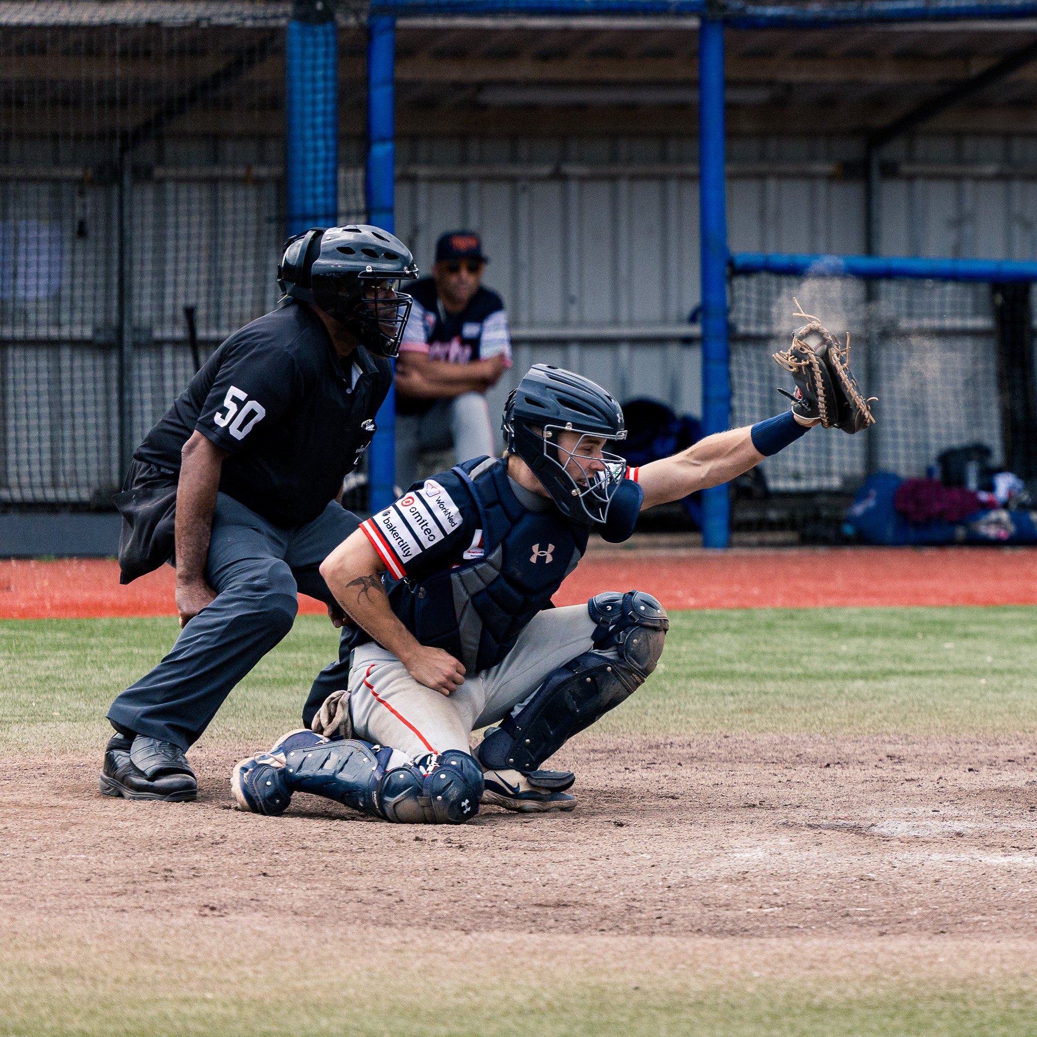 A baseball catcher diving to catch a ball, with an umpire behind him, on a baseball field.