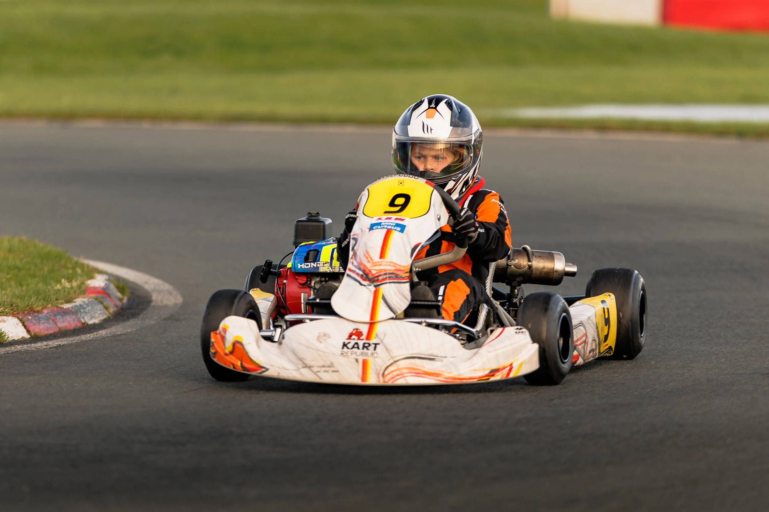 A young person driving a go-kart on a race track, wearing a helmet and racing suit.