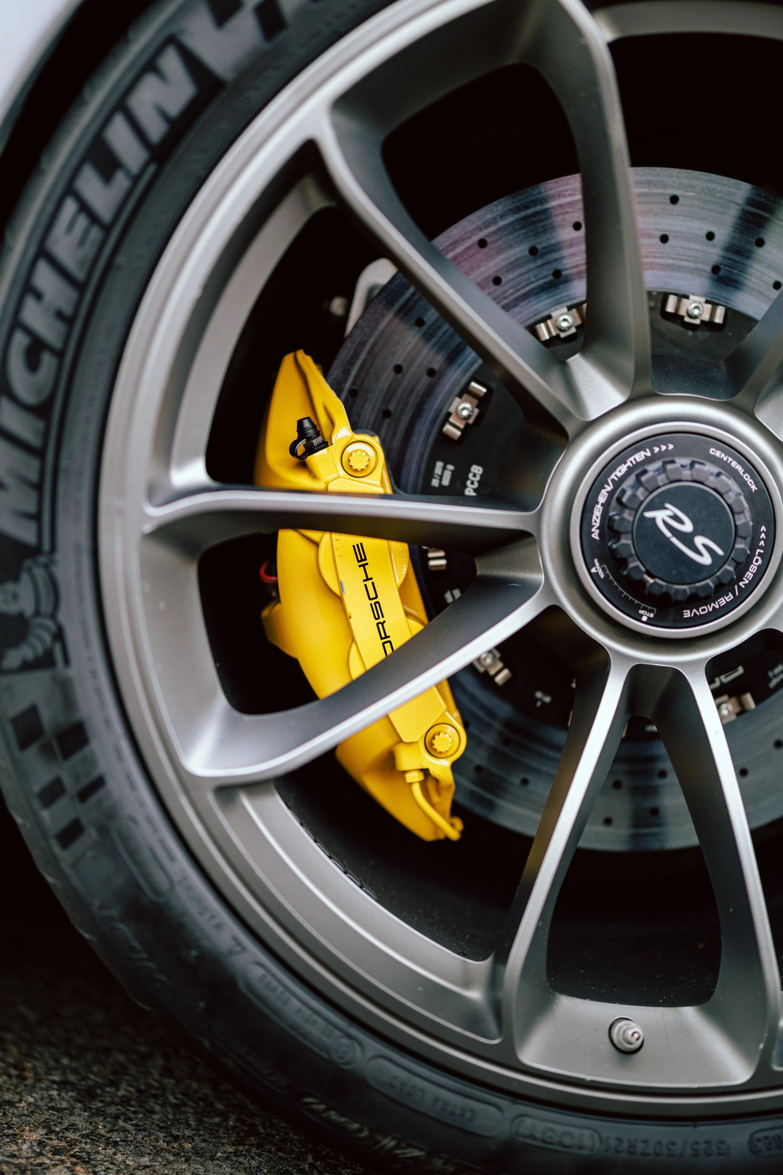 Close-up of a high-performance car wheel featuring a yellow Porsche brake caliper, ventilated brake disc, and Michelin tire.