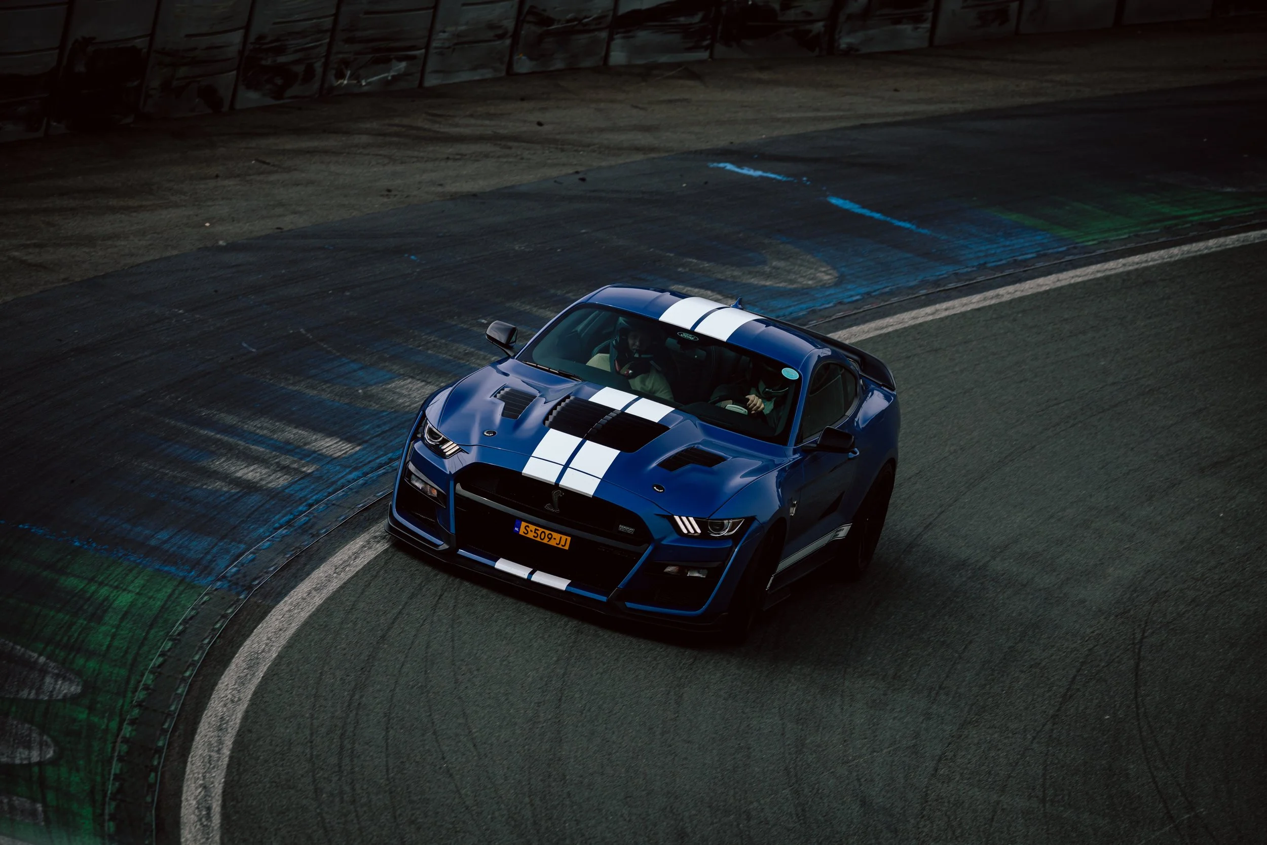 A blue sports car with white racing stripes on a racetrack, taking a sharp turn.