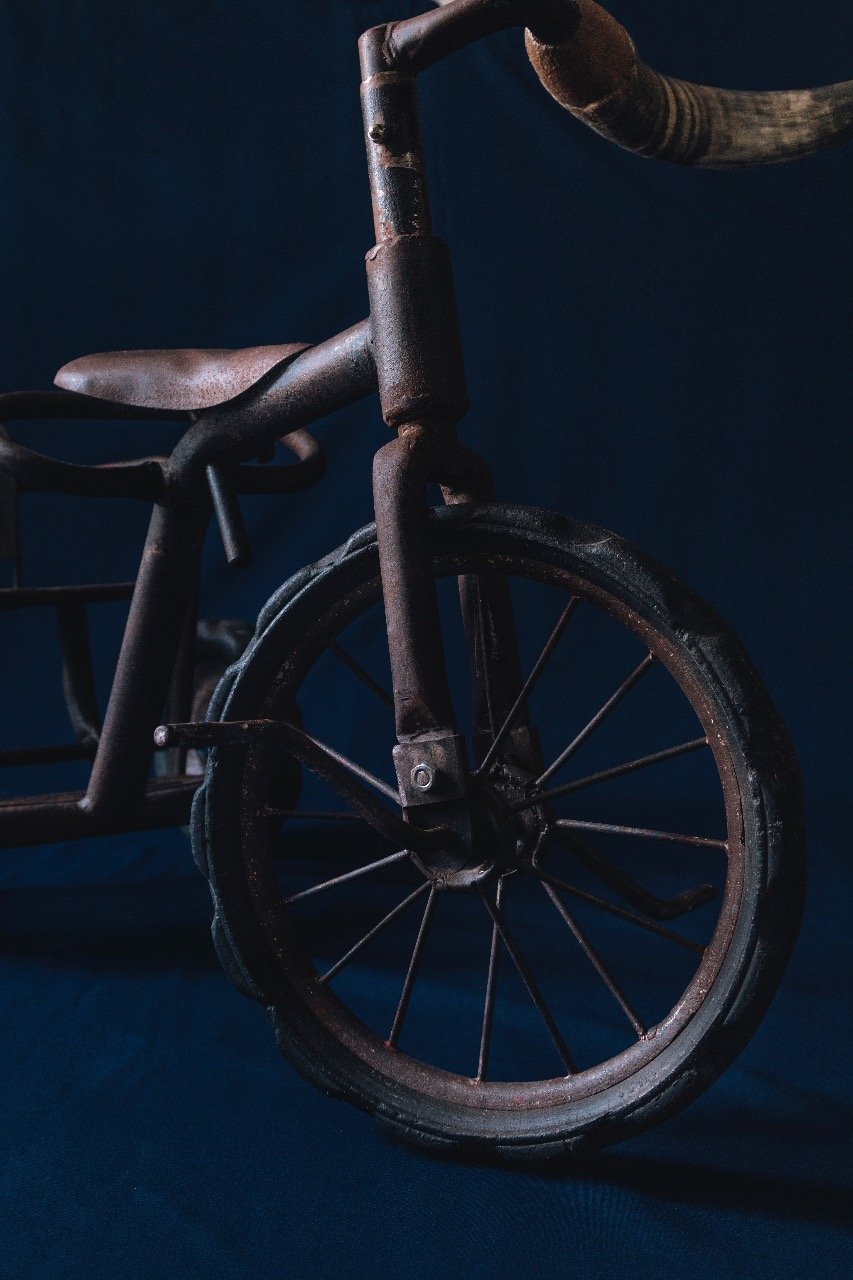 Close-up of an old, rusty tricycle with a dark background.