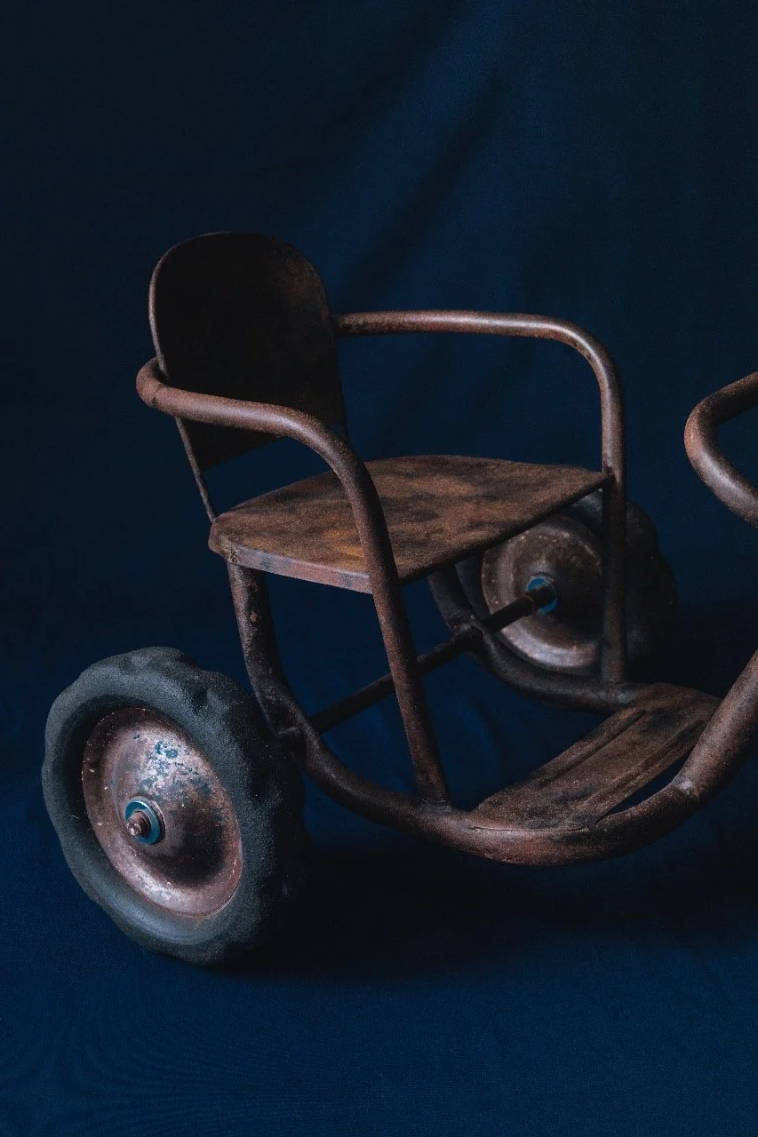 Old rusty tricycle with a child's seat and large wheels, set against a dark blue background.