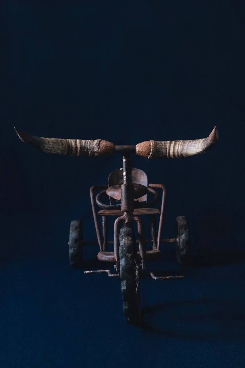 A vintage, rusted tricycle with large handlebar horns and a dark background.