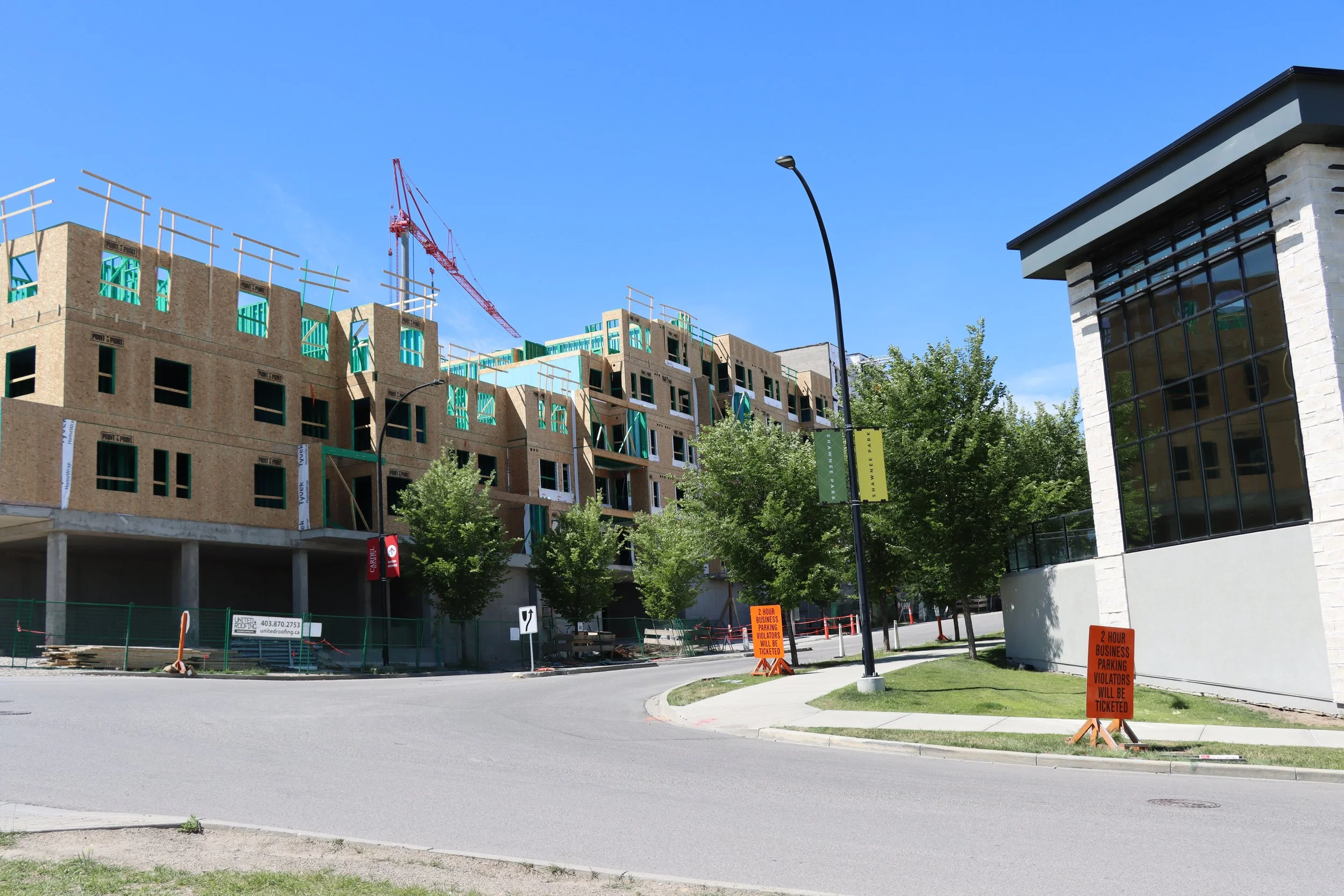 Construction site with partially built multi-story building, crane in the background, and orange signs indicating two-hour parking restrictions.