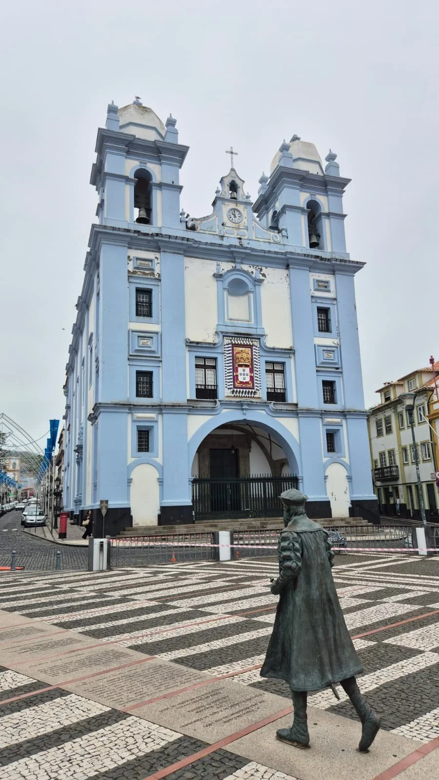Igreja azul e branca com duas torres e na frente a escultura em bronze de um homem