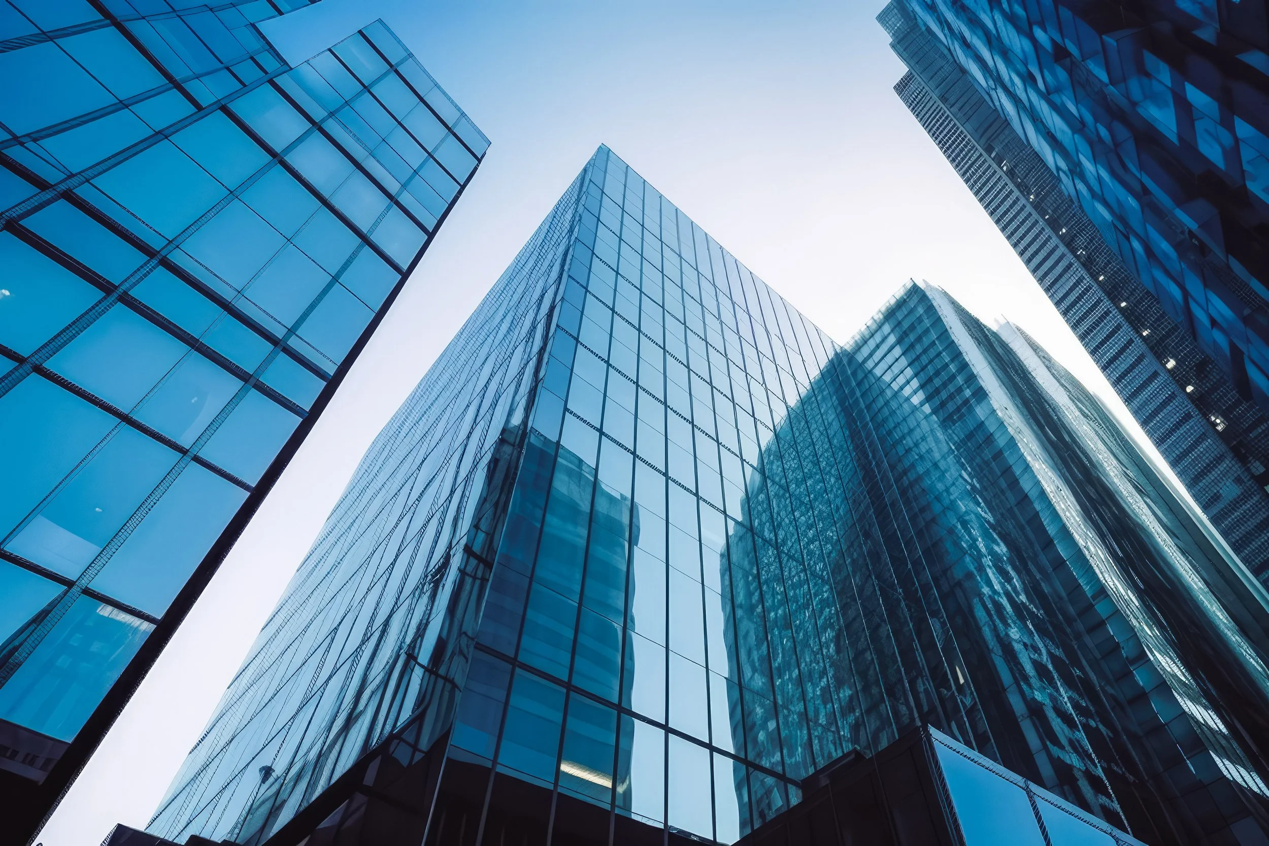 Looking up at modern skyscrapers with glass facades reflecting sunlight in a city skyline.
