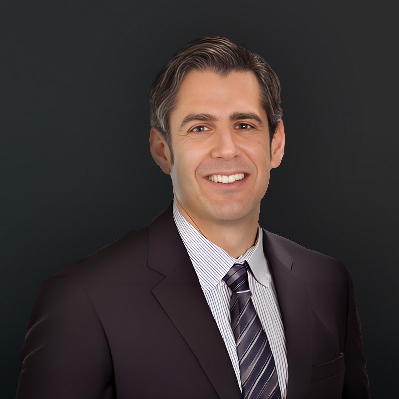 Professional portrait of a man wearing a dark suit, striped shirt, and tie, smiling against a dark background.